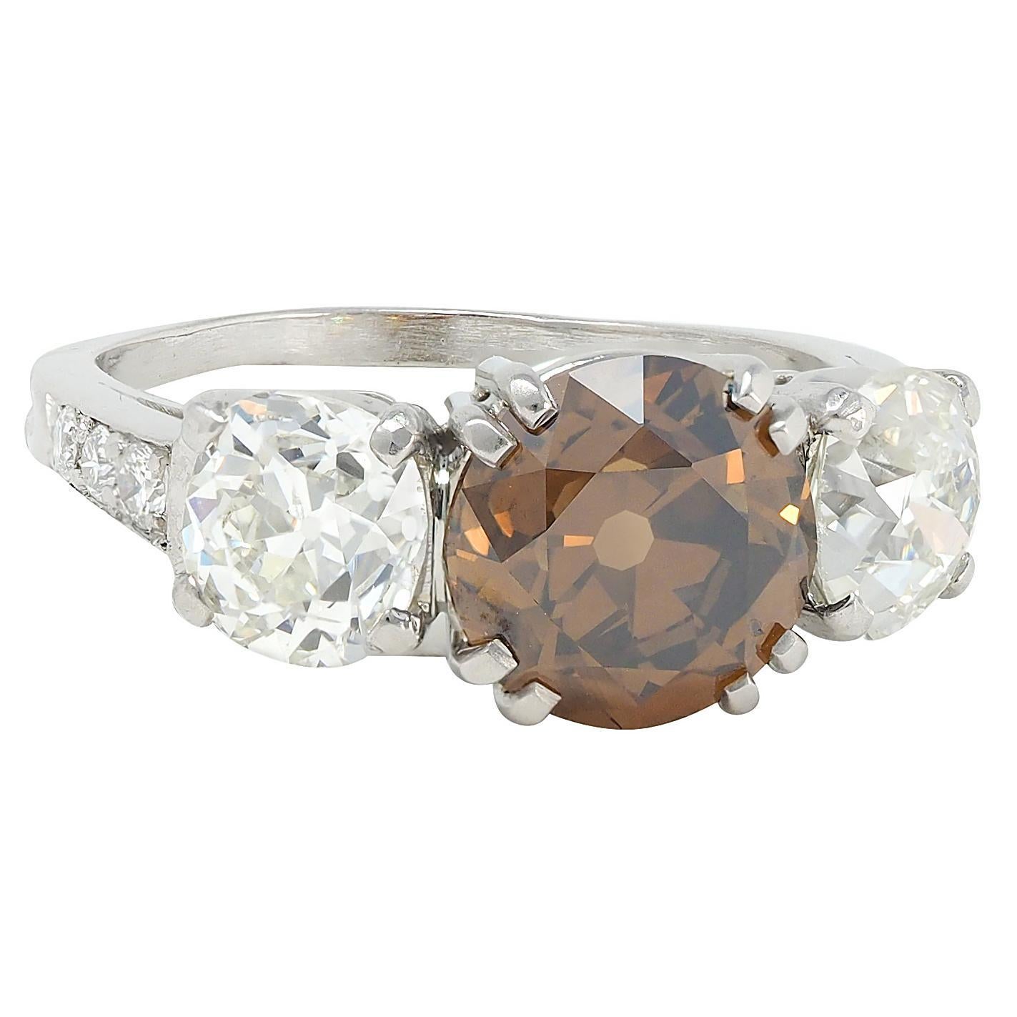 Centering an old European cut diamond weighing 2.45 carats - natural fancy dark orangy brown in color with VS2 clarity
Basket set via split prongs and flanked by cathedral shoulders prong set with old mine cut diamonds
Weighing approximately 1.70