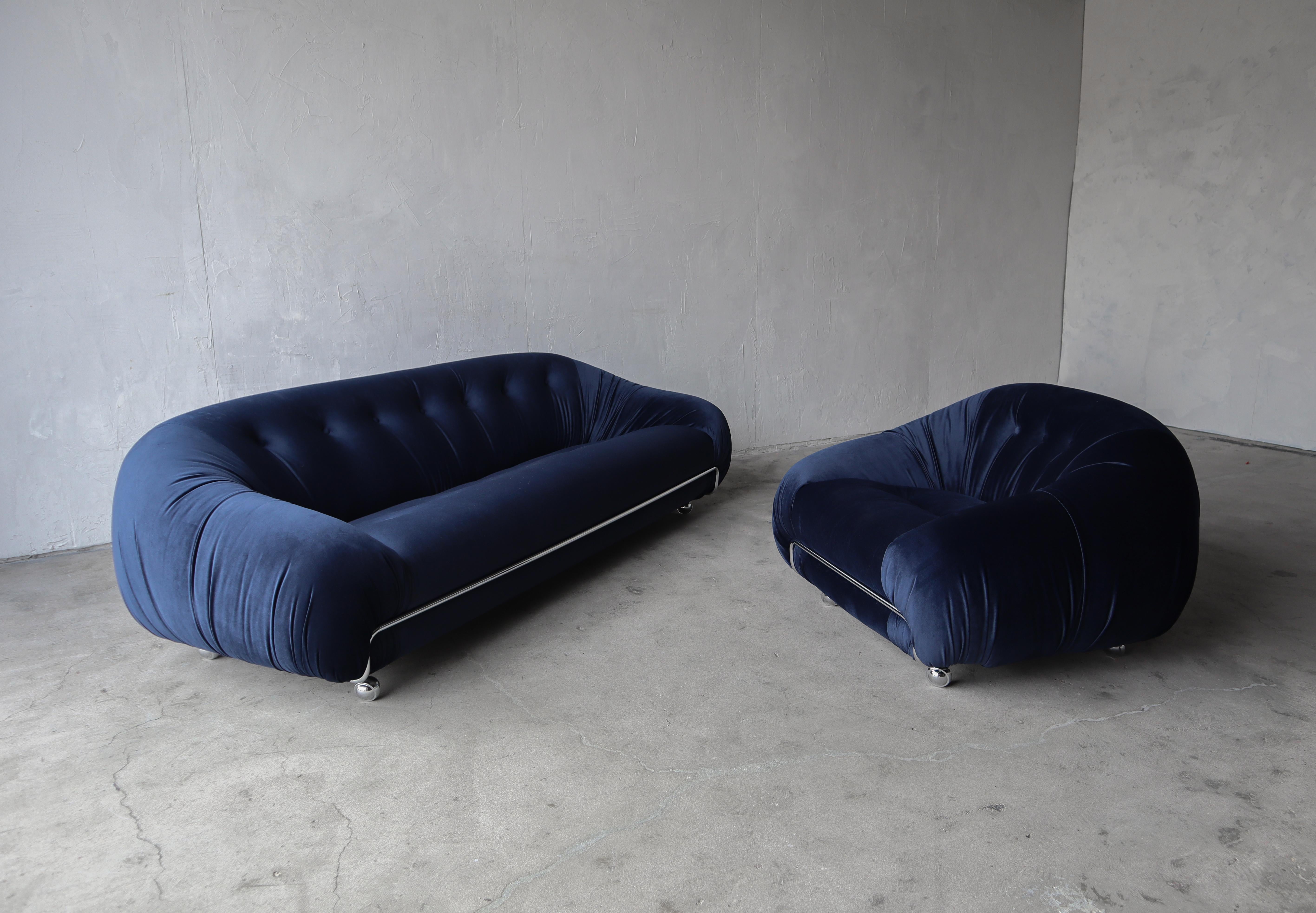Low and luxurious, this is truly a great 70s sofa and chair set. Dressed in all new deep navy blue velvet upholstery. The set features mirrored chrome trim and new 2