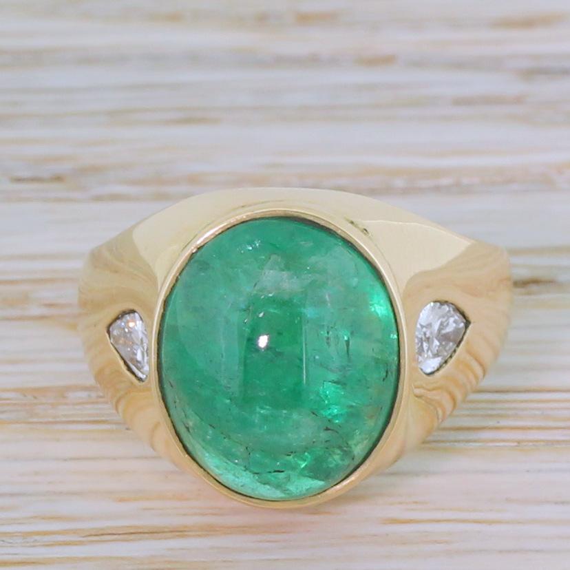 A glorious and glowing vintage emerald ring. The large oval shaped cabochon emerald displays a bright, verdant green and is secured within a sleek 18k yellow gold mount, adorned with a pair of high white pear brilliant cuts at the