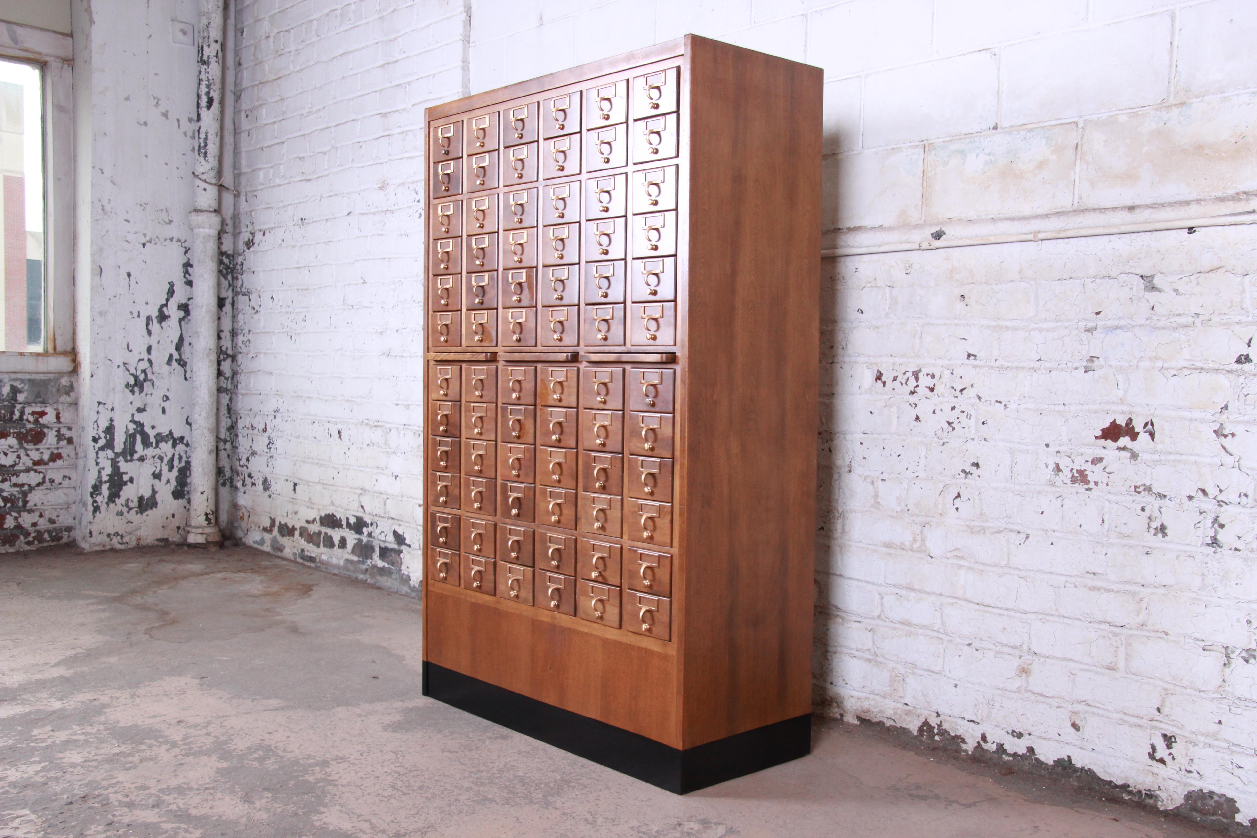 An exceptional midcentury library card catalog cabinet. The card catalog features beautiful wood grain and an amazing 72 dovetailed drawers. All of the drawers slide well, and they have adjustable dividers. There are three pull-out writing tablets,
