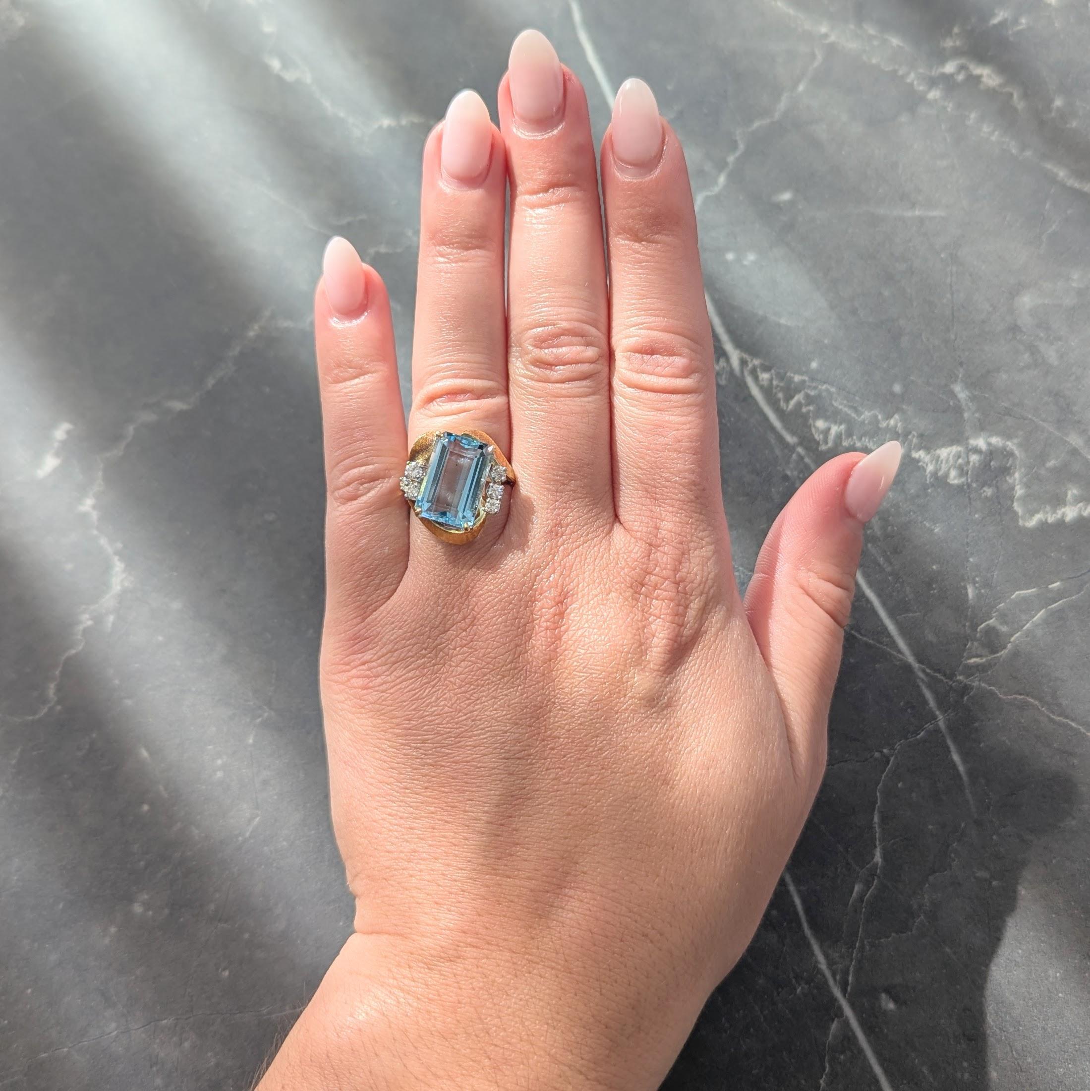 In der Mitte ein rechteckiger Aquamarin im Stufenschliff mit einem Gewicht von etwa 7.00 Karat
Transparent hellblau in Farbe und Zacken in Korb mit wirbelnden umgeben gesetzt
Bypass-Stil mit eingravierter linearer Textur und Diamanten im