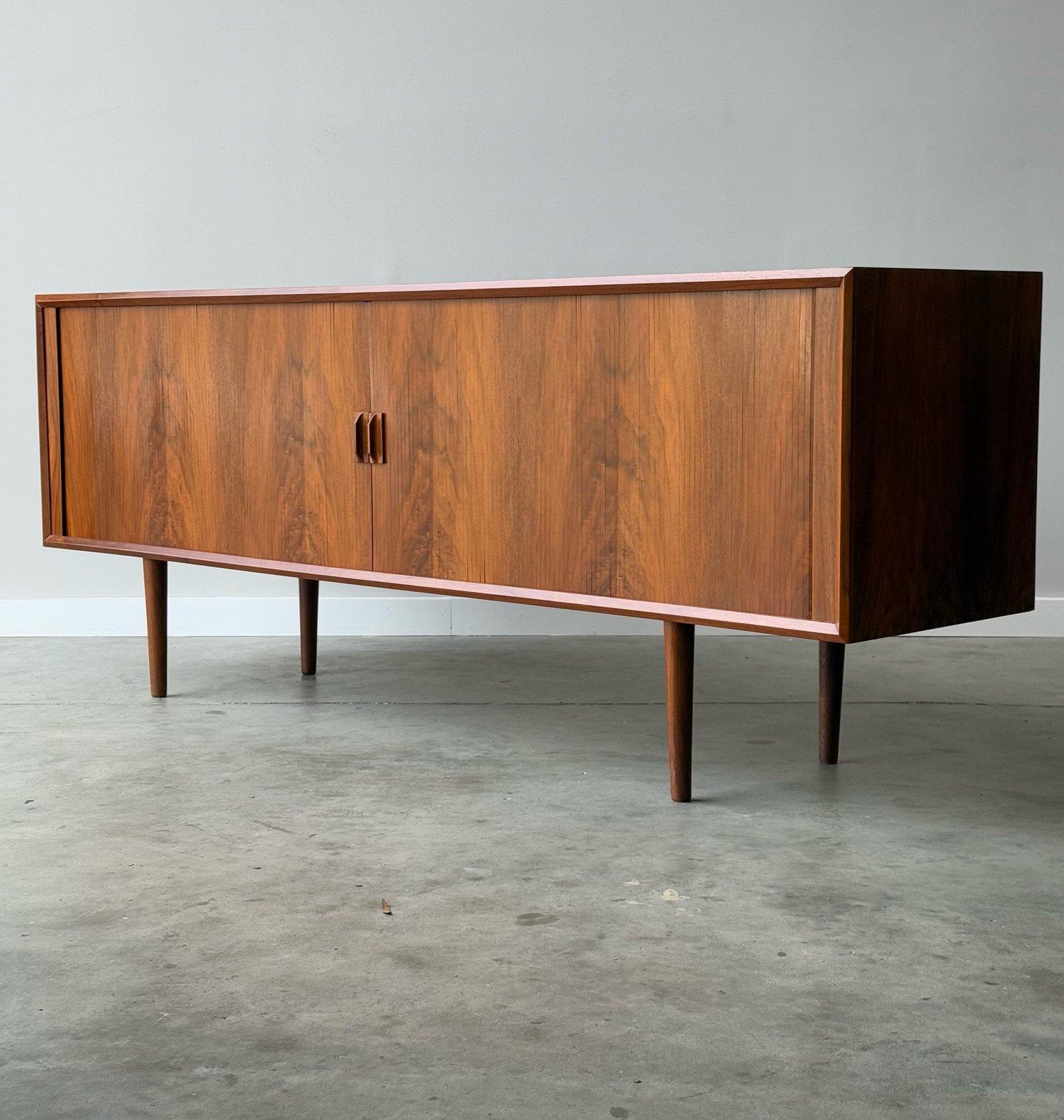 Mid-century credenza designed by Svend Aage Larsen, Denmark. Sleek profile featuring two smooth sliding tambour doors with sculpted handles and sits on tall tapered legs. We currently have two versions of this credenza, this is the smaller of the