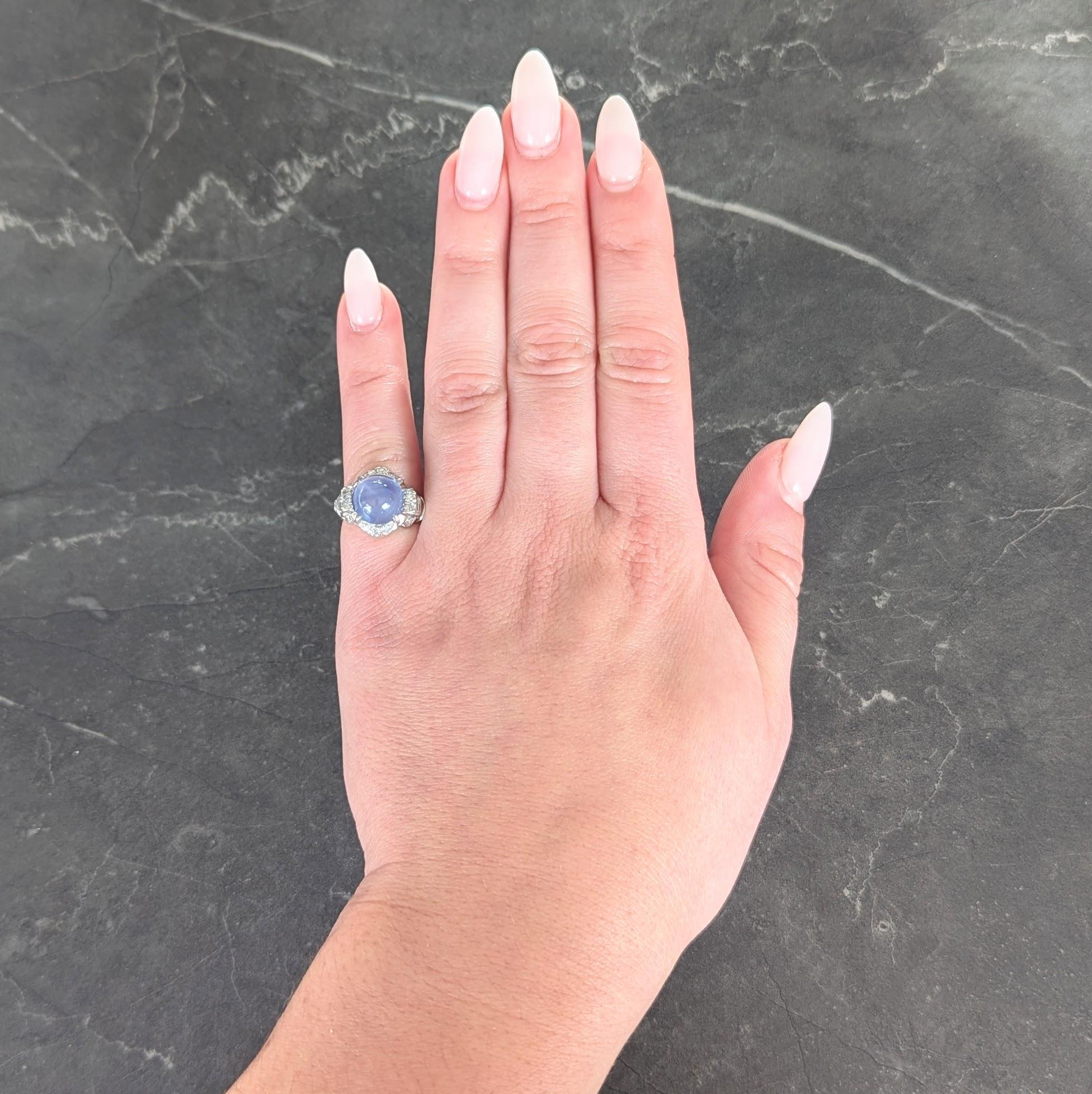 Centering a round shaped sapphire cabochon weighing approximately 7.88 carats total
Translucent light blue in color and displaying a six-rayed asterism
Prong set with a bombe surround and scrolling volute shoulders
Bead and flush set with single and