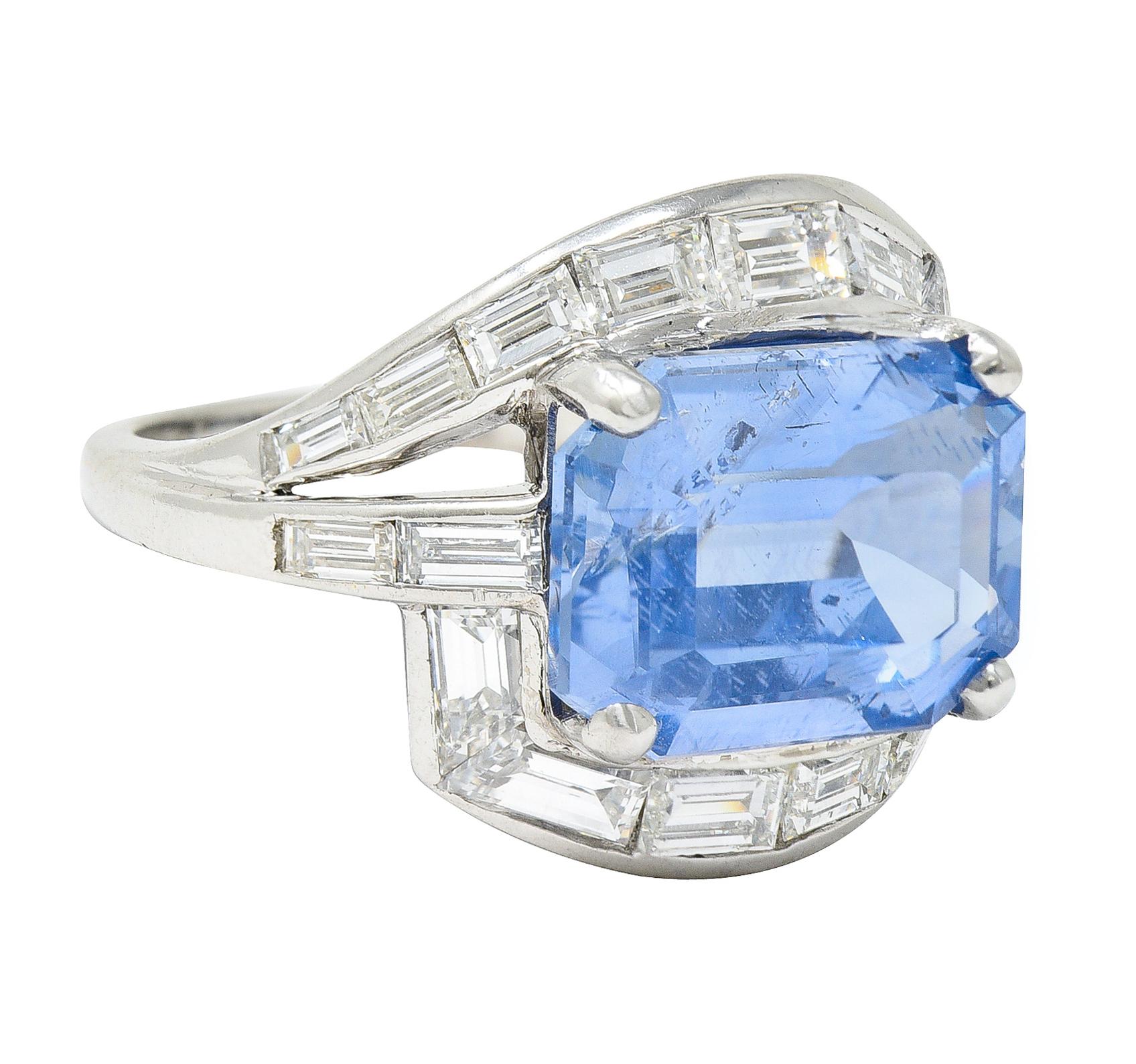 Bypass style ring features an emerald cut sapphire - set East to West. Weighing approximately 7.05 carats with medium light and slightly violetish blue color. Natural Ceylon in origin with no indications of heat treatment - encompassed by shoulders