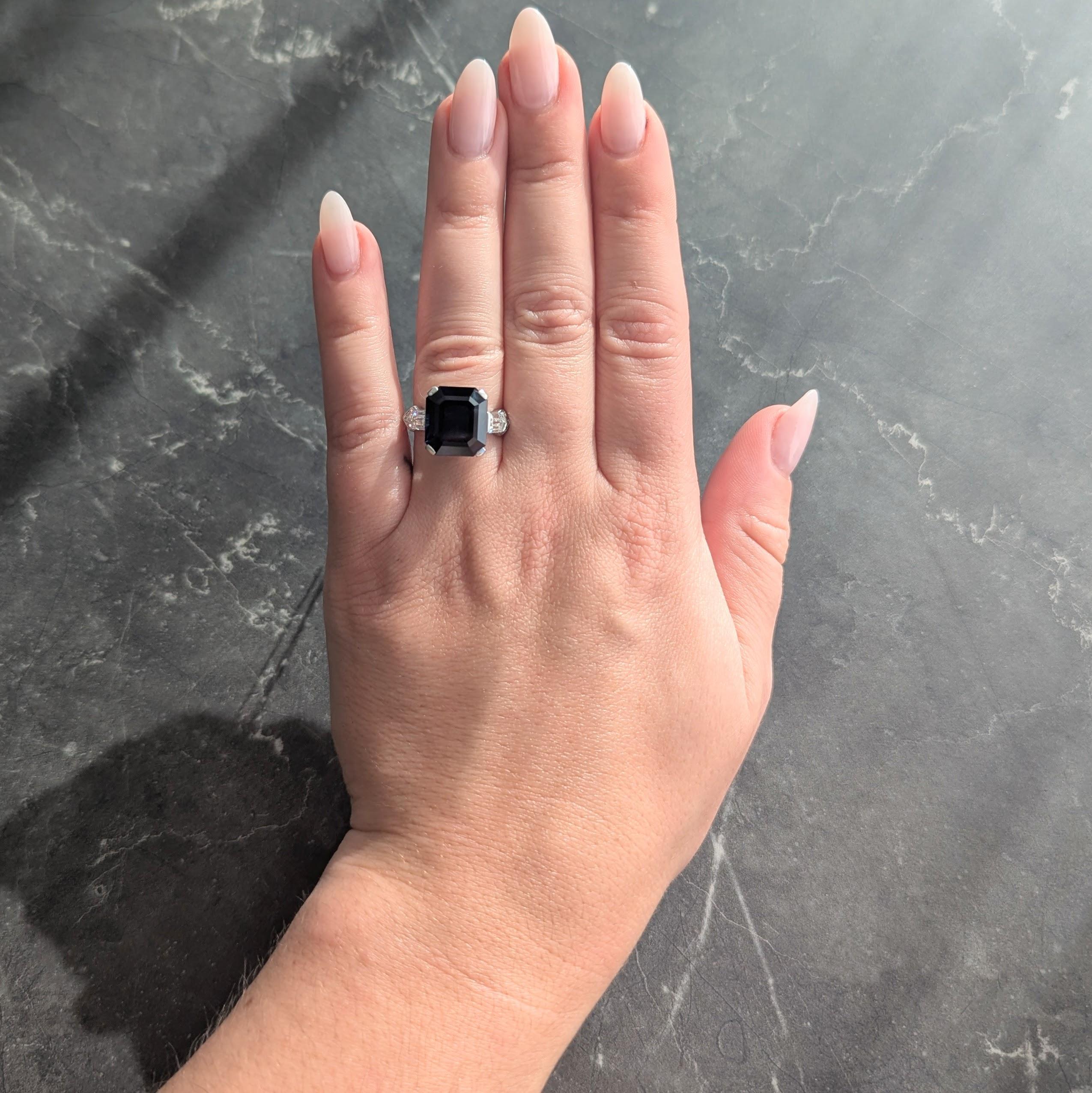 Centering an emerald cut sapphire weighing 8.82 carats - transparent deeply saturated blue in color
Natural Thai in origin and displaying no indications of heat treatment - prong set in fancy basket
Flanked by bullet cut diamonds weighing