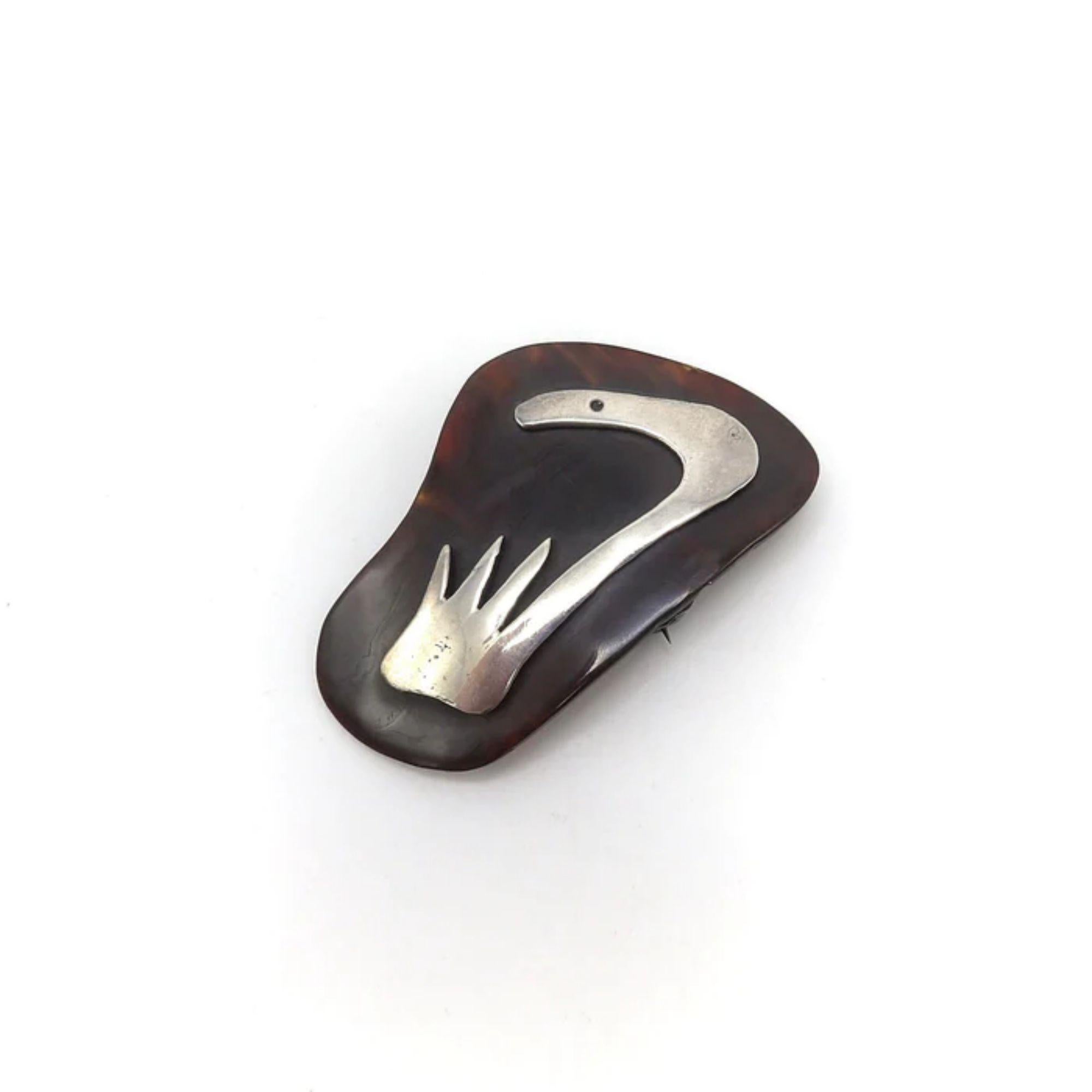 A striking Taxco, Mexico, brooch with an abstracted sterling silver design on a dark brown tortoise shell. The design leaves a lot to the imagination, looking a bit like a snake's head peaking out above some grass. The silver is cut graphically, and