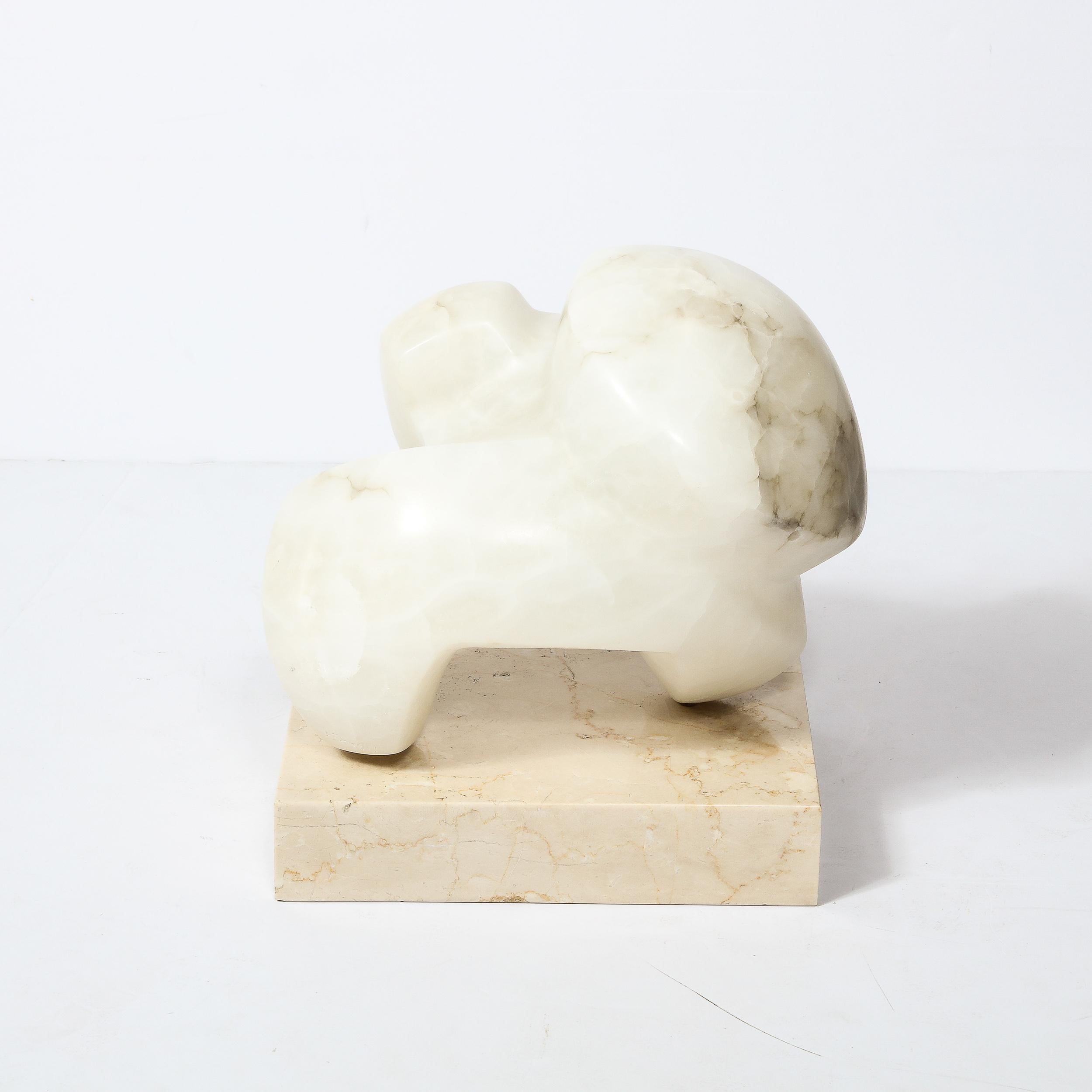 This Mid-Century Modernist Abstract Sculpture in Alabaster on a Marble base was created by the artist Julie Small Gambly in the United States Circa 1985. Featuring gorgeous veining in the alabaster and a rectilinear solid marble base, this
