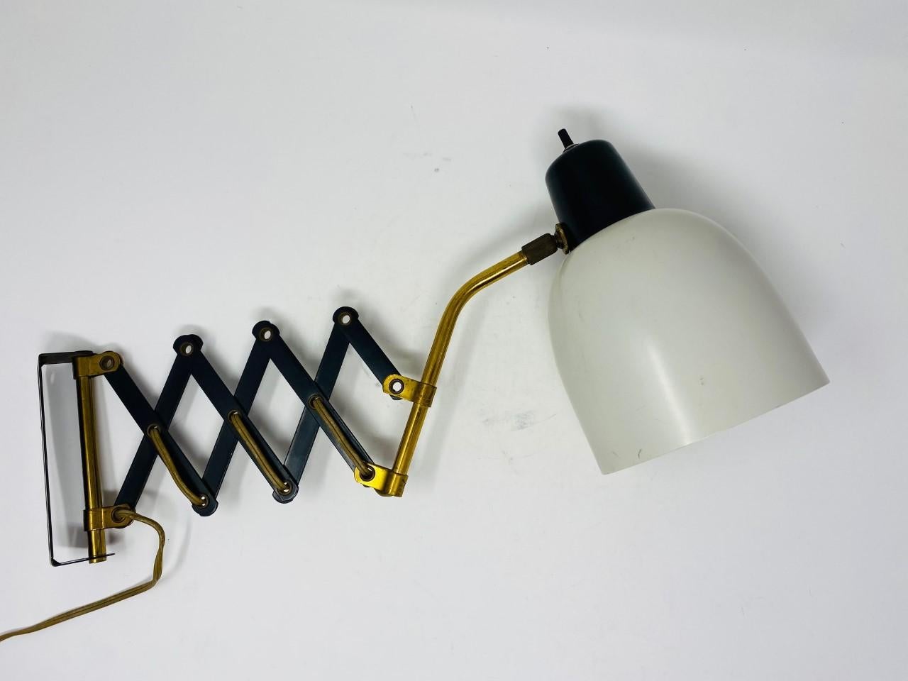 Stylish lamp sconce with accordion scissor arm. This is a great addition to any room where you want to add light without the need of space. This piece extends and contracts to facilitate your needs. It has a metal lampshade. The iron scissor arm is