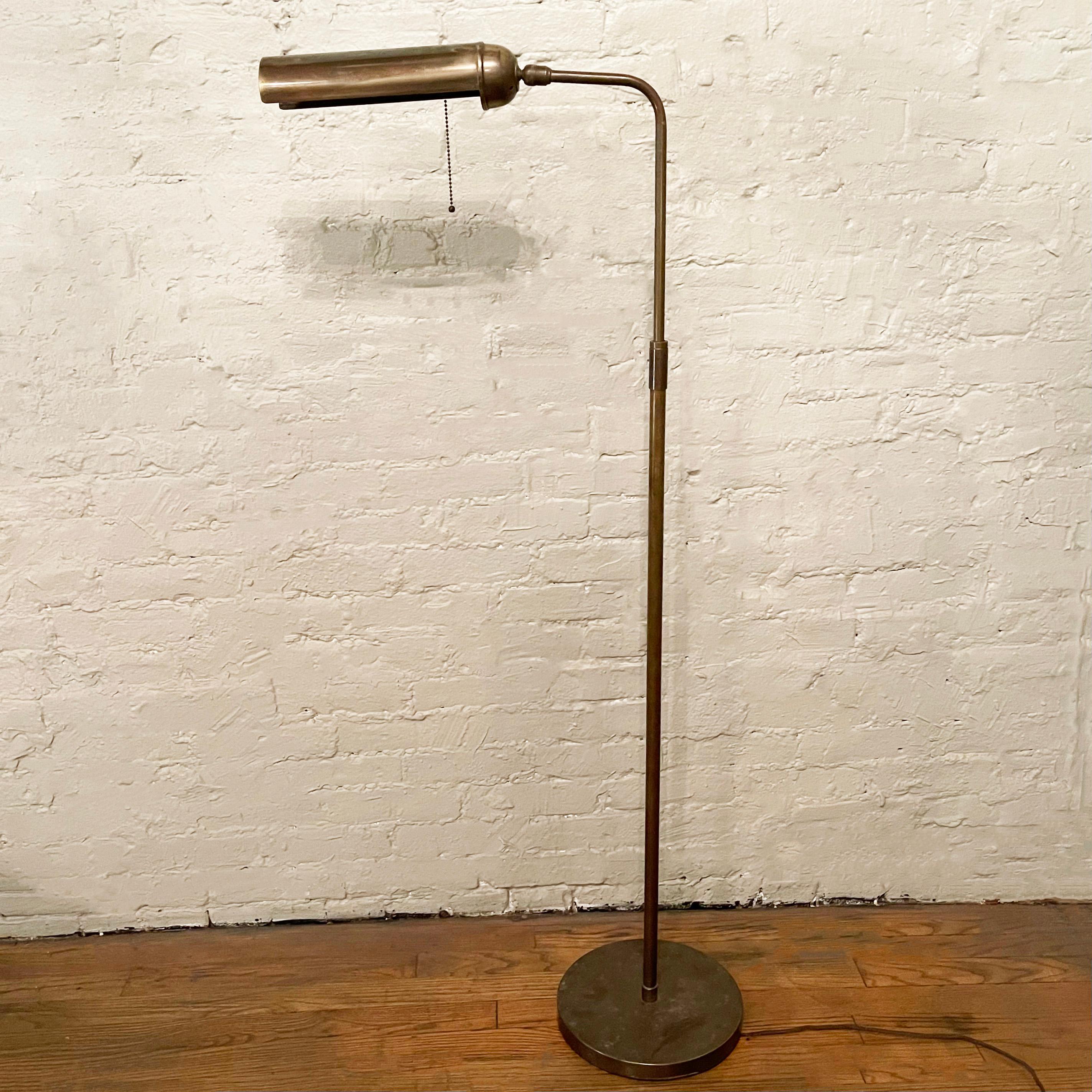 MId-century, patinated brass, library reading floor lamp features an adjustable, linear shade that pivots on a ball to cast light up, down or sideways with original pull chain switch and a telescopic stem to adjust the height from 50 - 56 inches.
