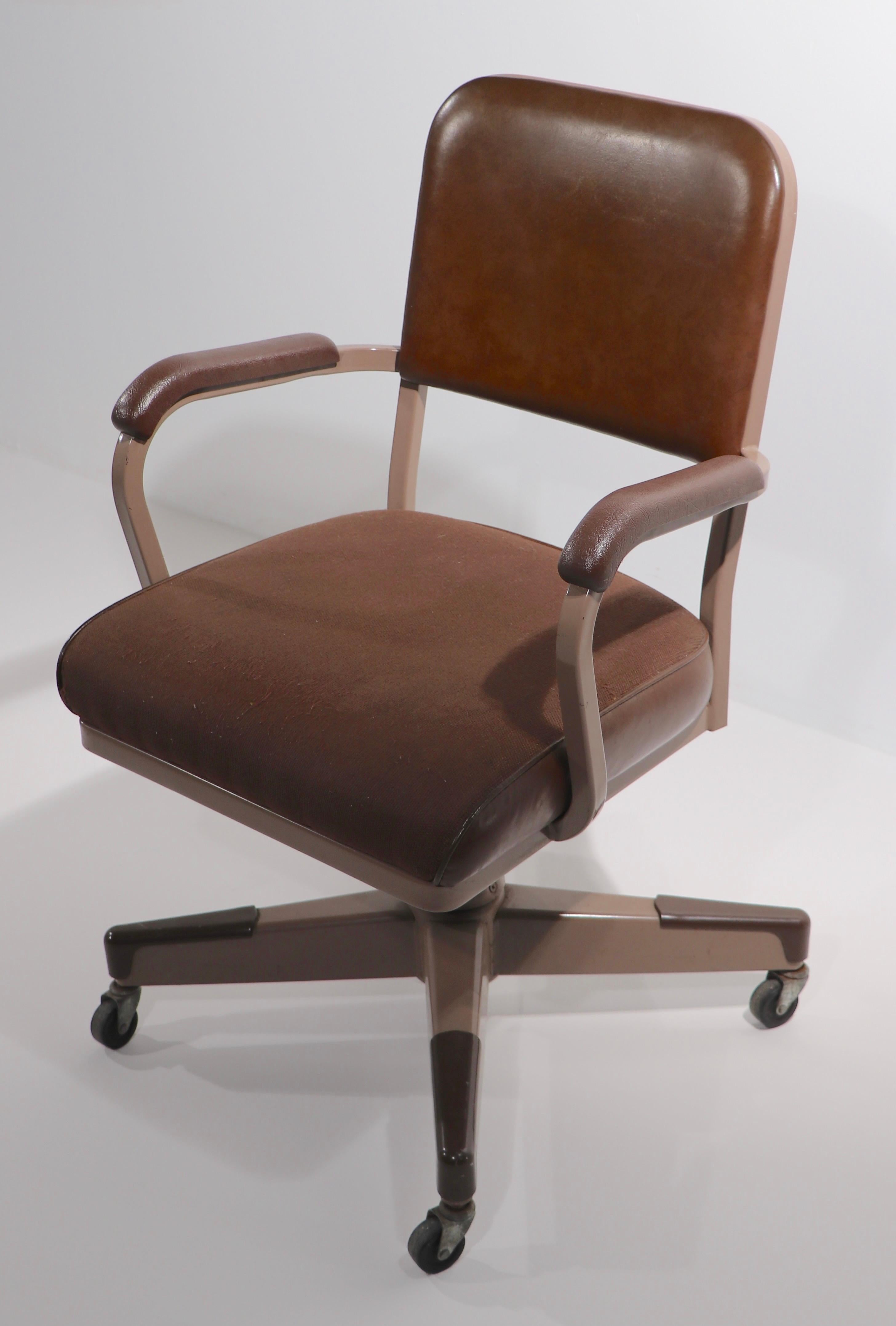 Mid century swivel, tilt office, desk chair in very fine, original condition, clean and ready to use. The chair has a light brown metal frame with darker brown seats back and arm rests. The seat rotates, and tilts, the base is on wheels, the seat is