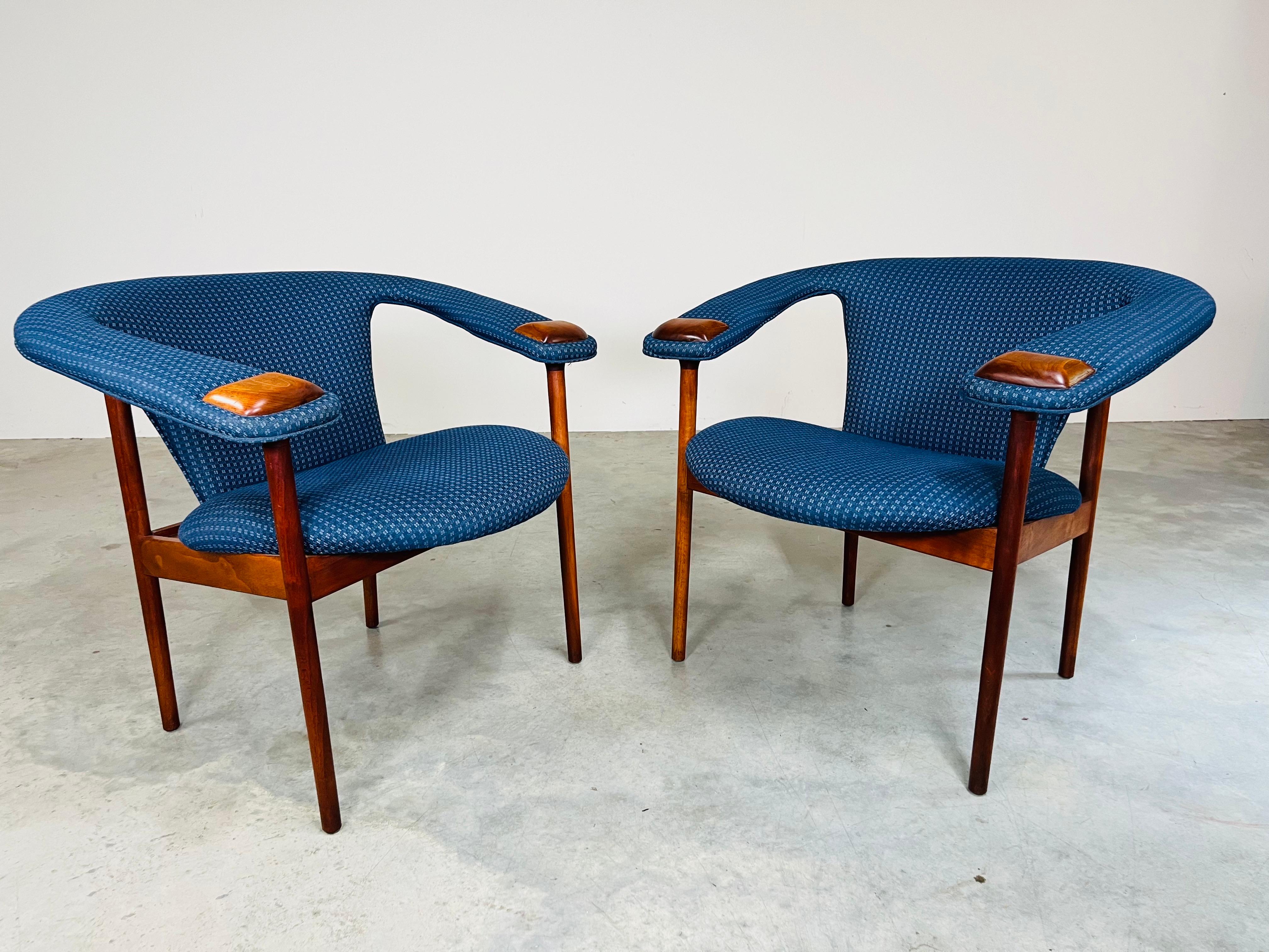Rara coppia di poltroncine con schienale a spiovente della metà del secolo scorso, con struttura in noce e zampe di appoggio in noce abbinate e tappezzeria in misto cotone/polietilene a fantasia blu. Circa 1968. 
In ottime condizioni, con