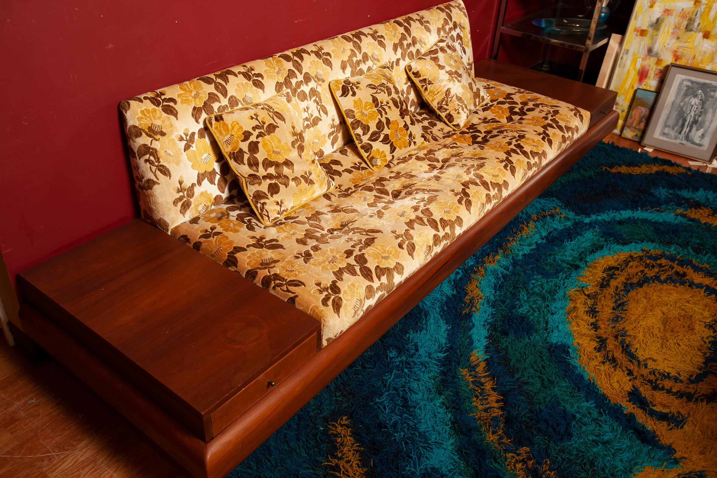Super rare and groovy this sofa is in amazing original condition. Midcentury at its max. Original flower and leaf velour upholstery in gold and brown on a beige background with 3 matching toss cushions. Attached walnut drawers on each side match
