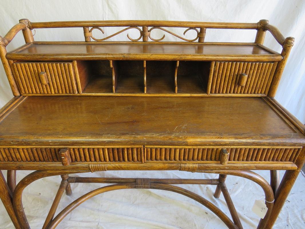 Mid century Aesthetic Revival bamboo writing desk, circa 1950s, having a bamboo three-quarter open gallery with central scrolls, atop a frieze with four pigeon holes flanked by two rattan facade drawers, behind a rectangular writing surface with