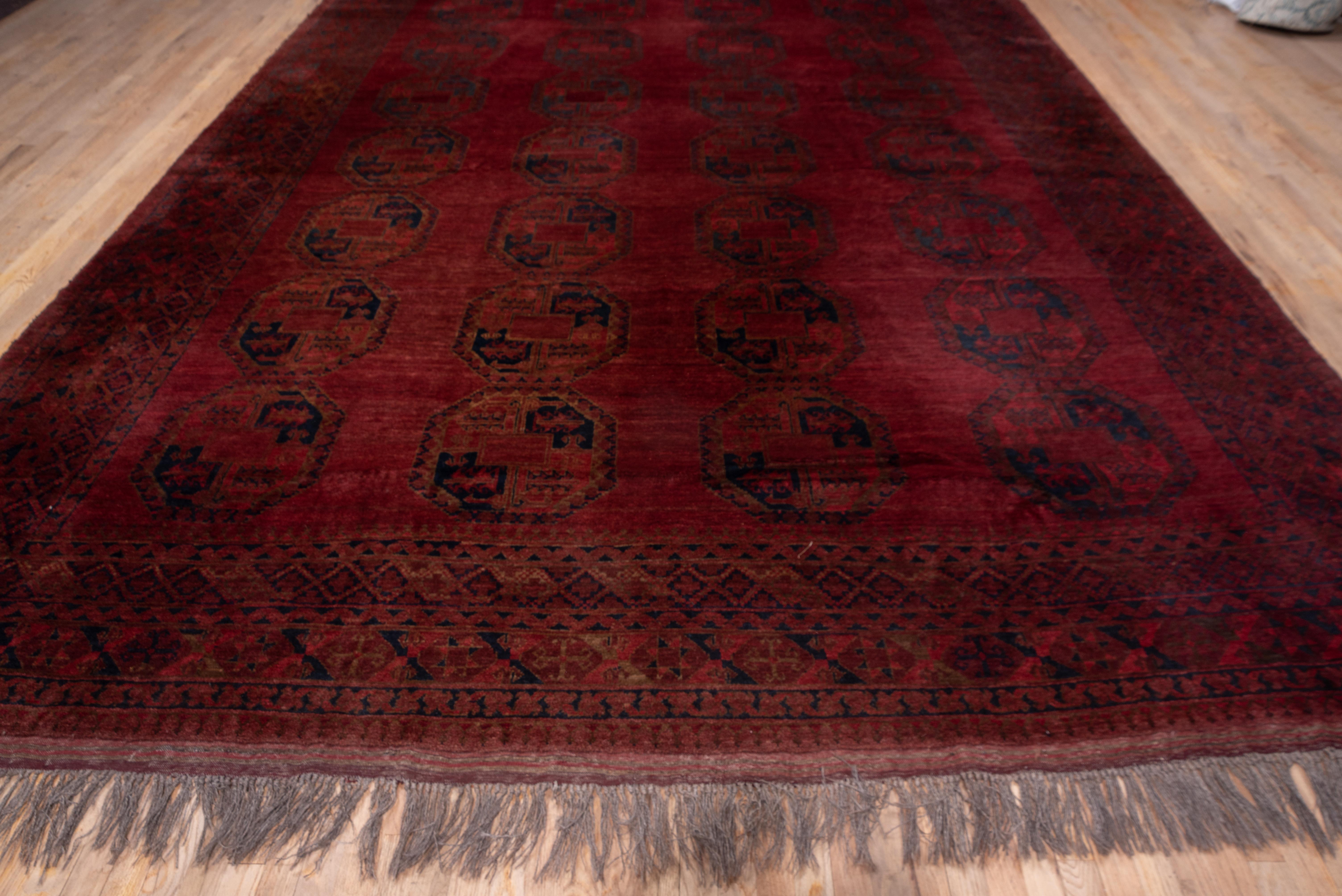 This nomadic Turkmen carpet shows four columns of characteristic tribal octagonal guls detailed in navy and red, set against the dark wine red, abrashed ground. At each end is a flat-woven dark red band. The condition is excellent with resilient