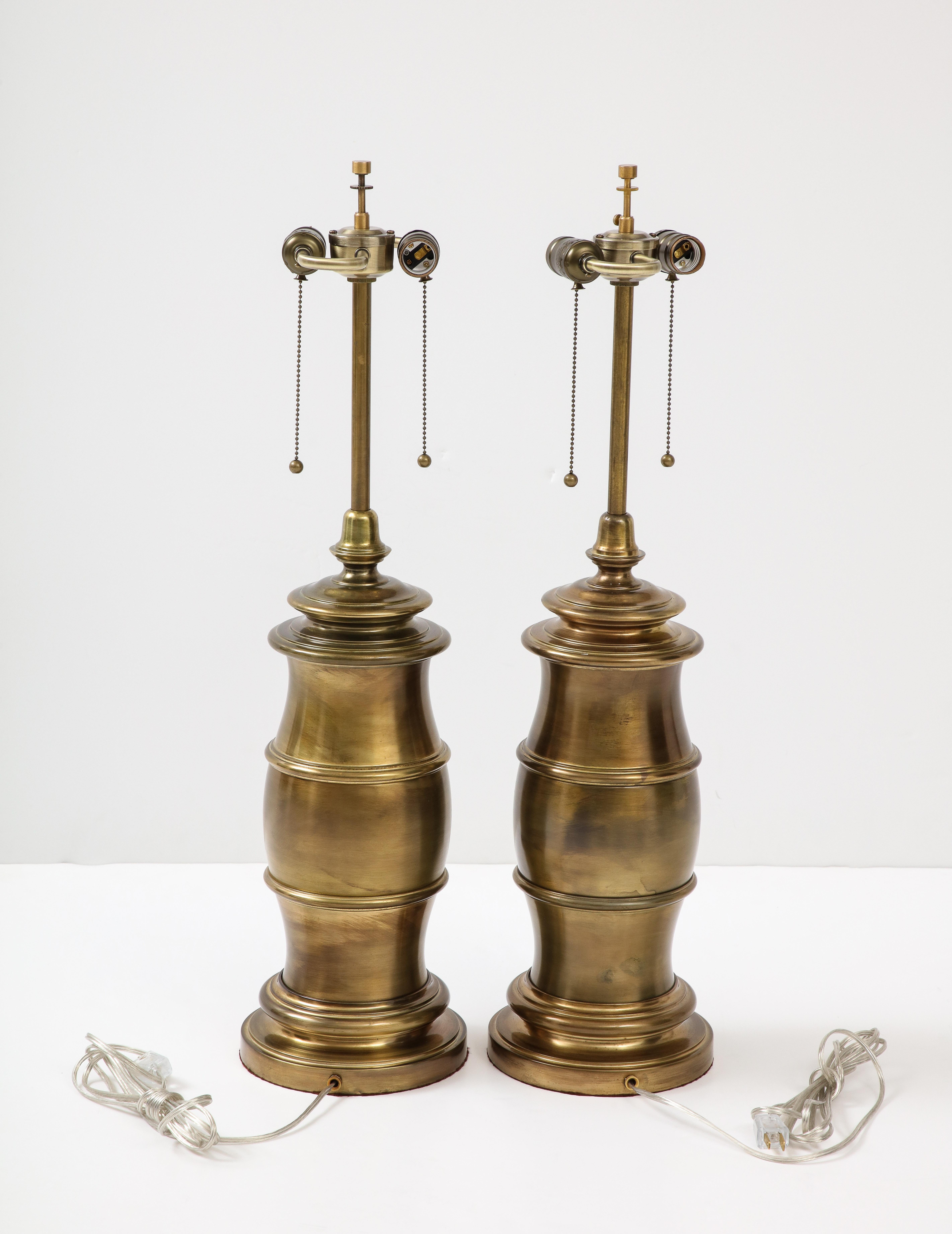 Ein Paar großformatige, stilisierte Lampen in Form eines Fasses, die in dunkler Bronze ausgeführt sind. Die Lampen wurden für den Gebrauch in den USA umverdrahtet, jede Fassung kann eine Glühbirne mit maximal 75 W aufnehmen.