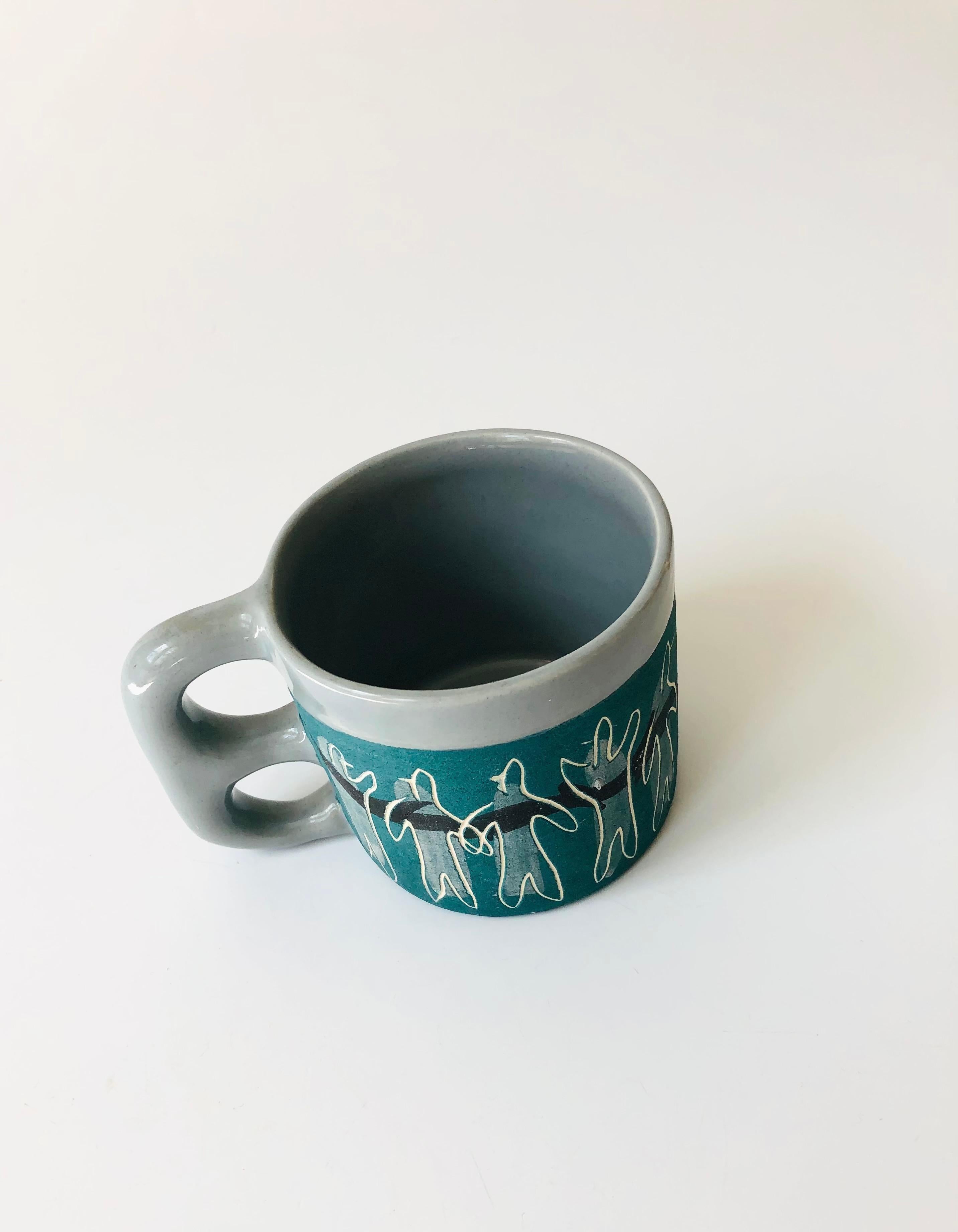 A wonderful midcentury studio pottery mug from the 1940s-1950s by ceramicist, Alice Smith of California. Decorated with a series of figures carved into the sides of the mug. Finished in a matte green glaze with a glossy gray glaze at the handle,
