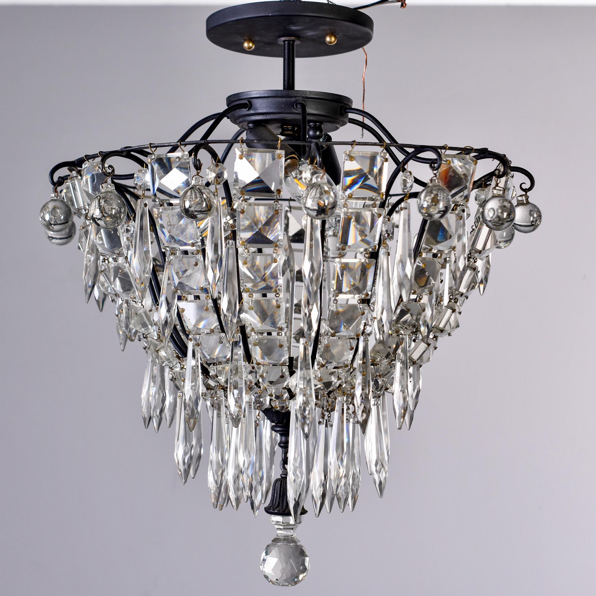 Semi-flushmount fixture features a black metal basket-form frame has a top row of clear crystal spears and draped with square, faceted crystals and crystal spears with a faceted crystal finial, circa 1950s. Three internal candelabra sized sockets.