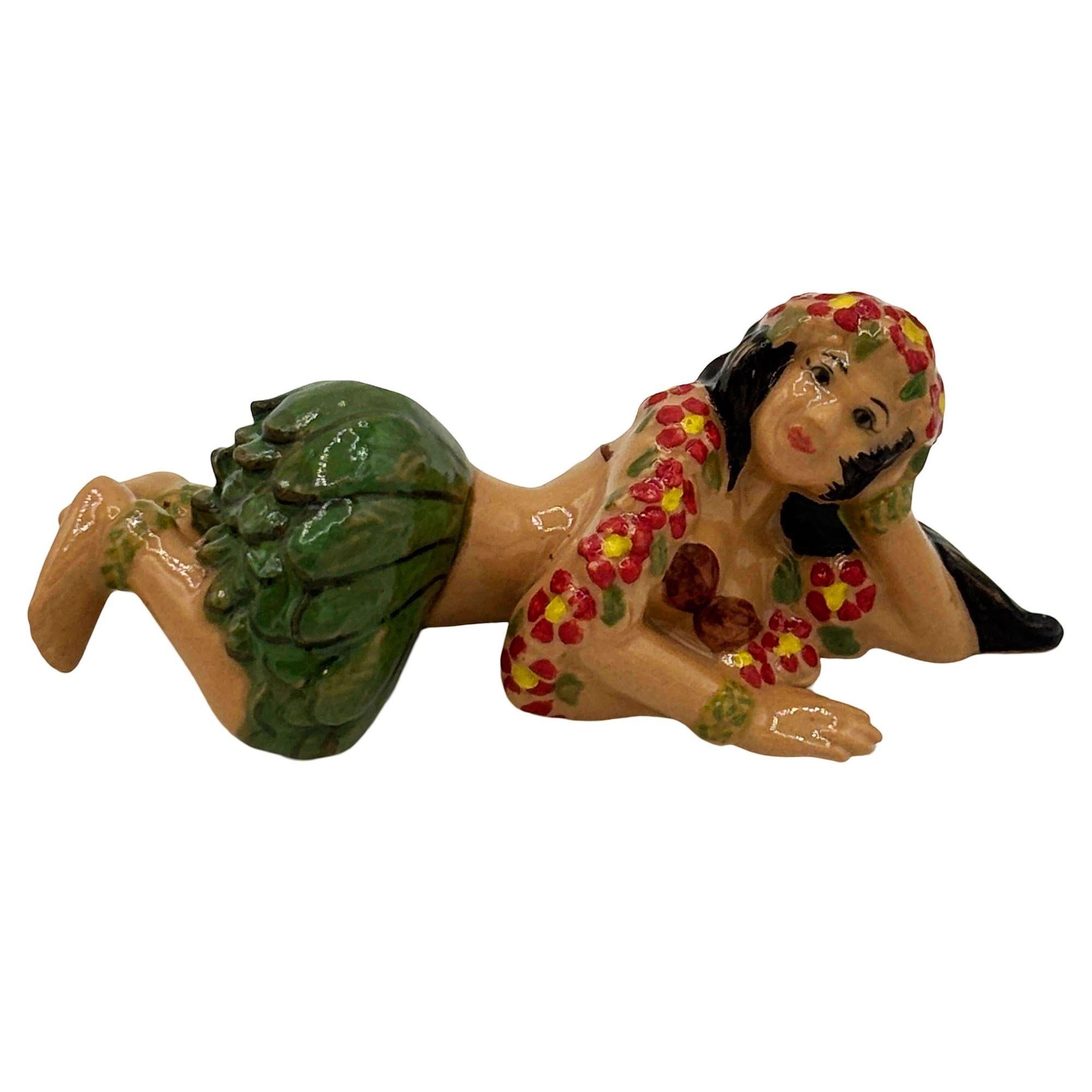 Figurina in ceramica della ragazza Hula di metà secolo sdraiata con fiori rossi e gonna di erba verde. La statua presenta una ragazza hula splendidamente dettagliata che guarda l'osservatore con uno sguardo dolce. La finitura lucida mette in risalto