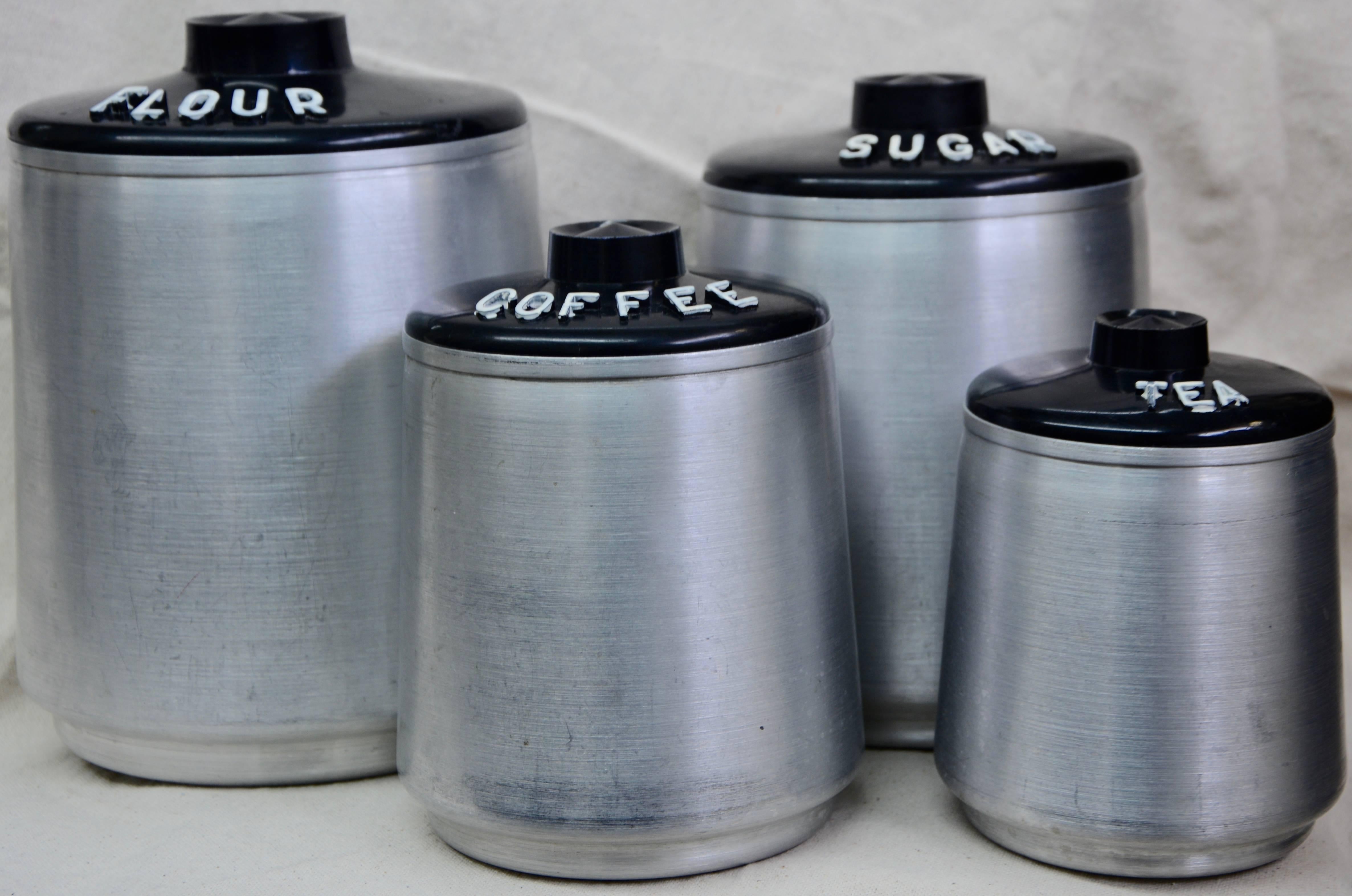 We are offering a vintage, midcentury Kromex by Alcoa brushed aluminium canister set. The canisters feature black plastic lids marked flour, sugar, tea, and coffee. Each lid is marked on the underside, Kromex. The words are highlighted in
