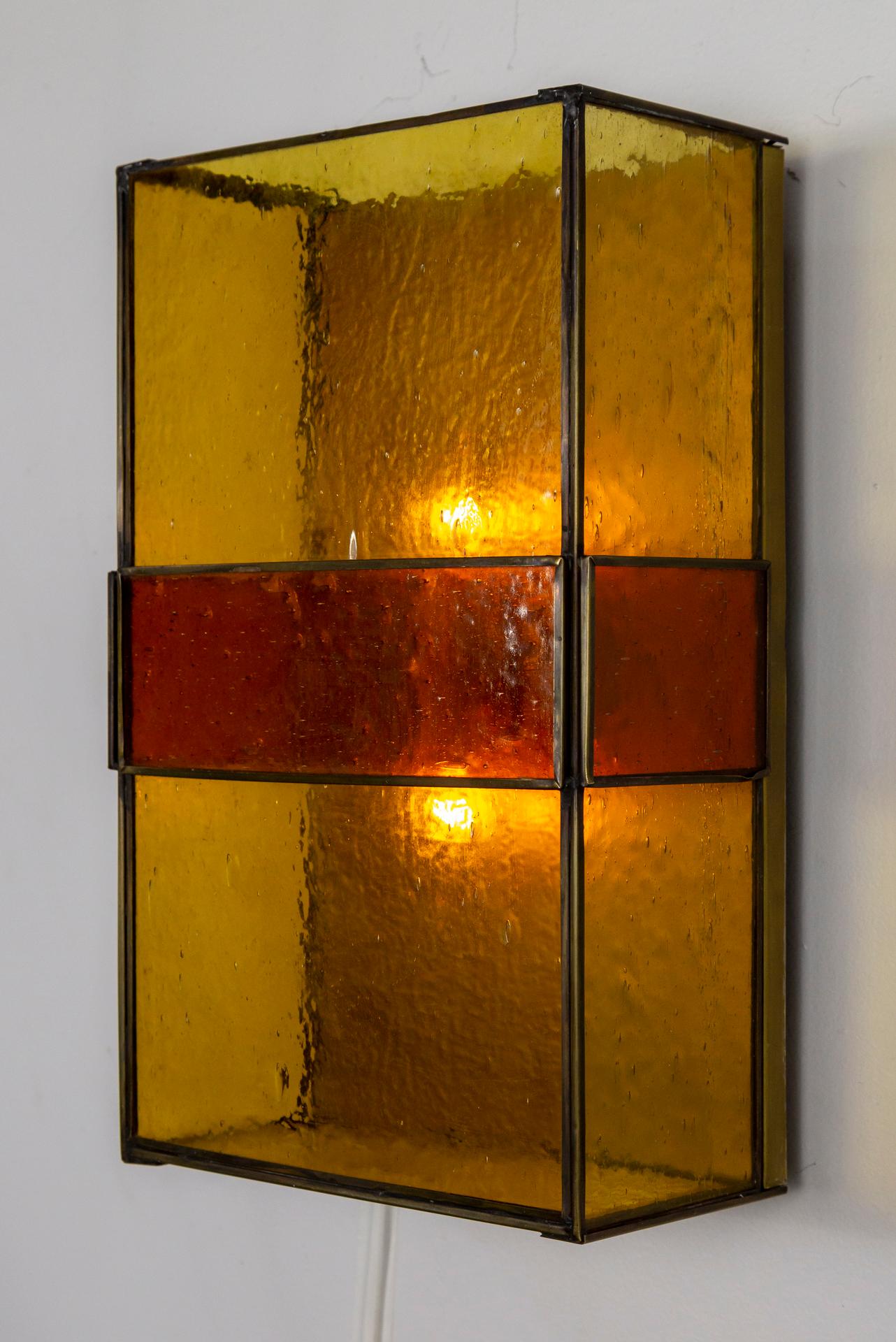 A late, mid century, stained glass and brass sconce with a pair of matching shallow pendants (semi flush mounts). Quality made, with clean, simple design and welcoming glow when lit. The sconce is a flat, yellow-amber rectangle with a rust-red panel