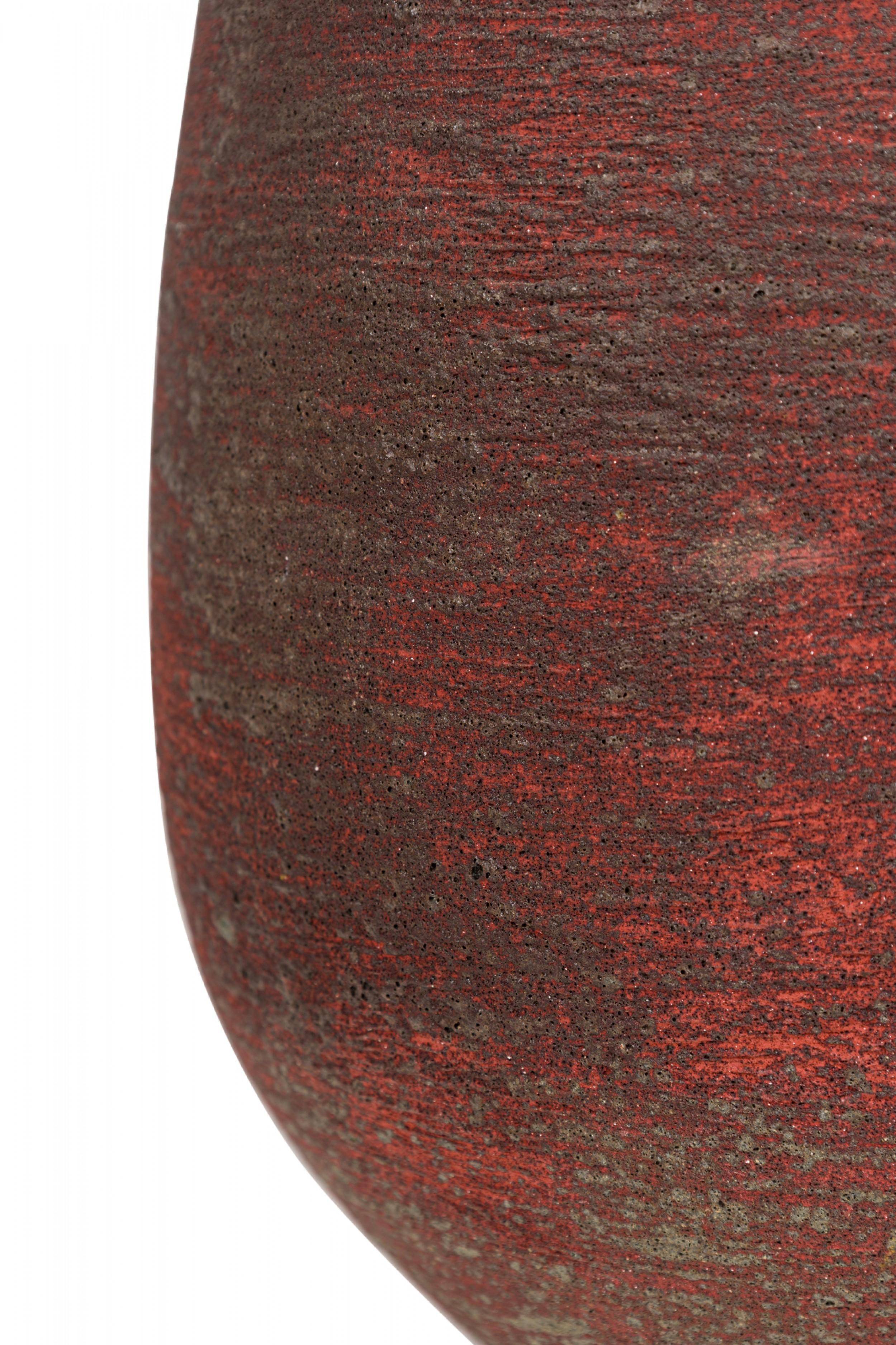 Lampe de table en céramique américaine du milieu du siècle, texturée horizontalement et cuite dans une glaçure rouge brique, de forme organique ovoïde effilée, surmontée d'une tige en laiton et d'un épi de faîtage en forme de boule, de deux prises