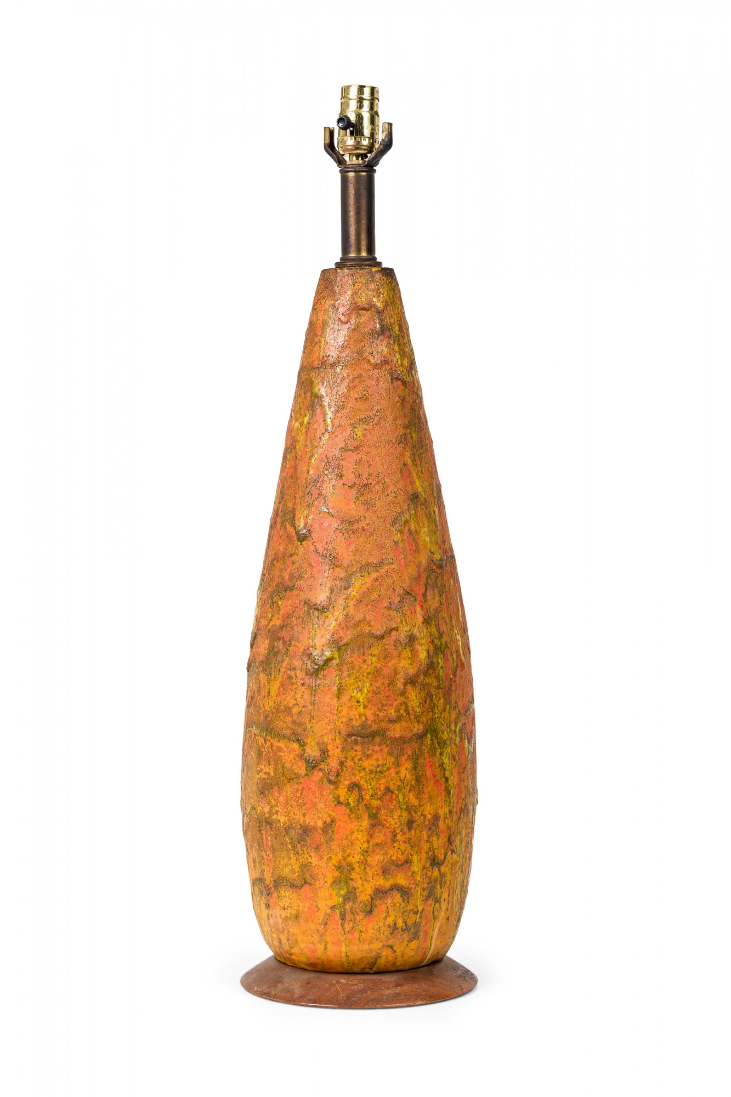 Mid-Century American ceramic cone form table lamp tapered toward the top, housing a brass stem with functioning light switch socket, the body bathed in a thick fat lava-style drip glaze over glaze in fiery orange and red gradations, mounted on a