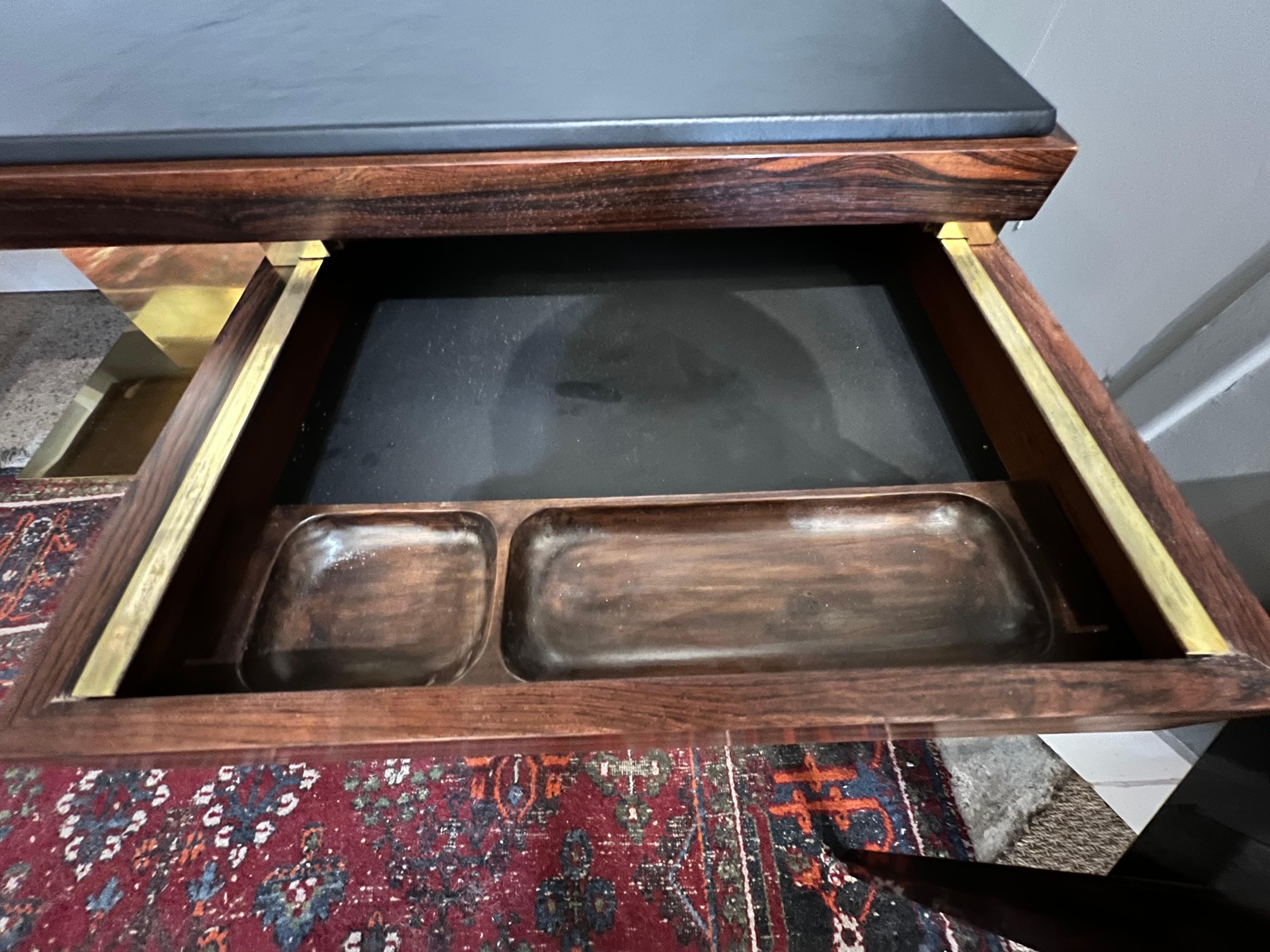 Der Schreibtisch ist aus Zebraholz gefertigt. Die Tischplatte ist mit braunem Rindsleder neu gepolstert. Auf der linken Seite befindet sich eine breite Schublade für Akten und auf der rechten Seite eine kleinere Schublade. Der Schreibtisch wird
