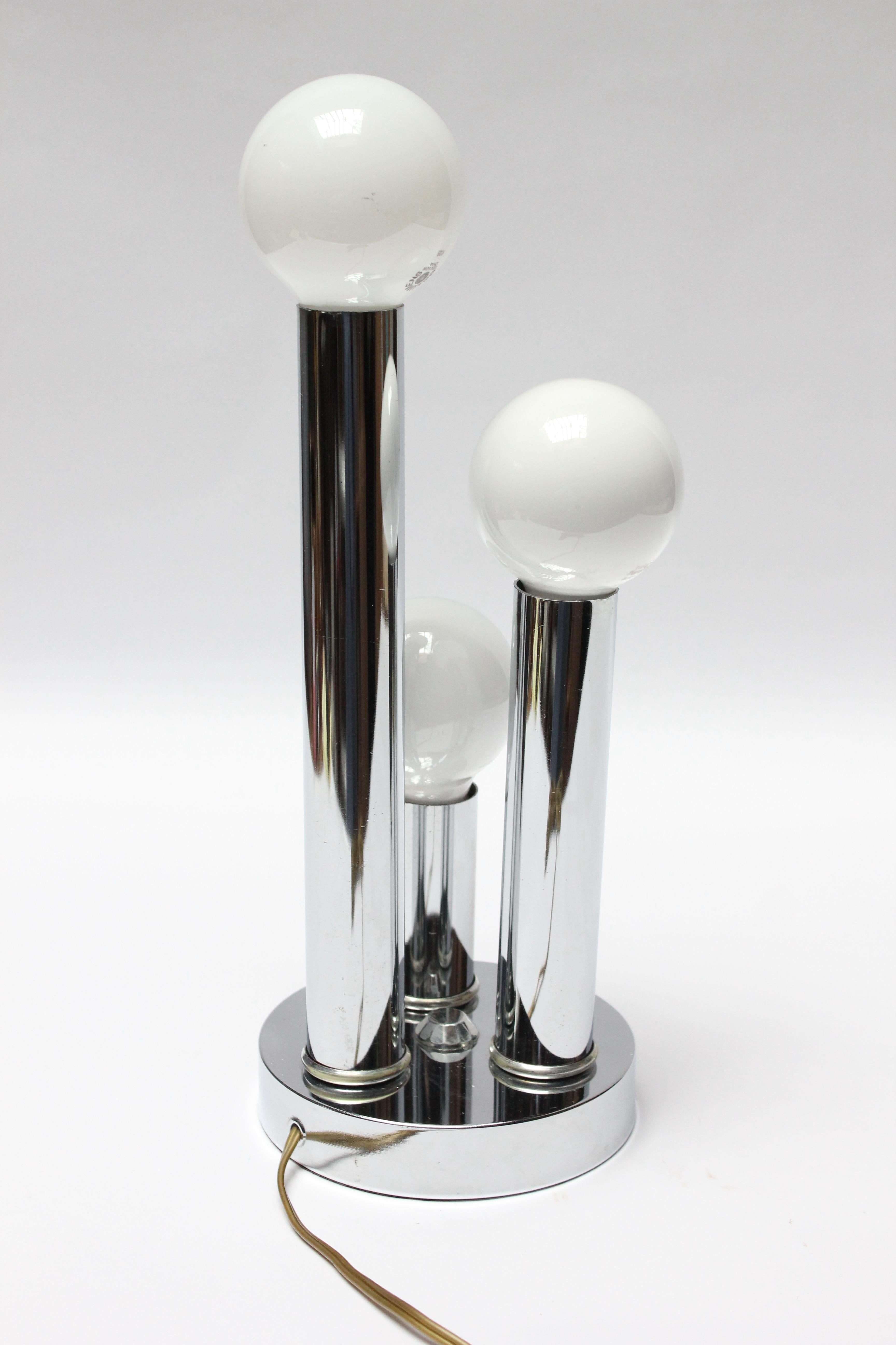 Mid-century three fixture/3-way lamp with three elongated cylindrical chrome pillars supported by a round base. Orb bulbs can be replaced, if another shape is desired. 
Light wear present to the polished chrome; overall, very good, vintage
