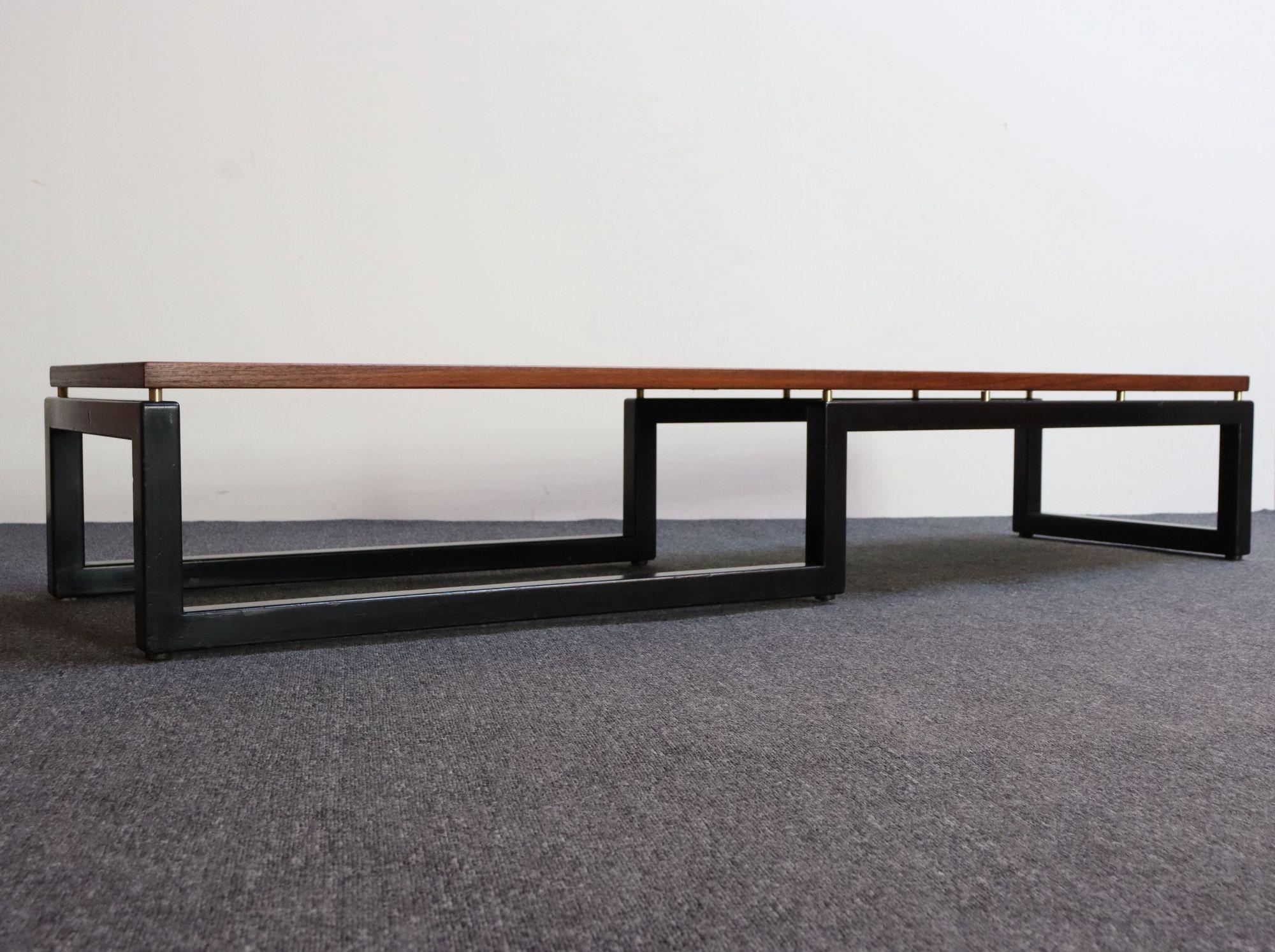 Sculptural low and and long coffee table/bench designed by Paul Tuttle, Michael Taylor, and Winsor White for Baker Furniture's New World Group (c.1953, USA).
Composed of an ebonized architectural base supporting a sold teak top via cylindrical brass