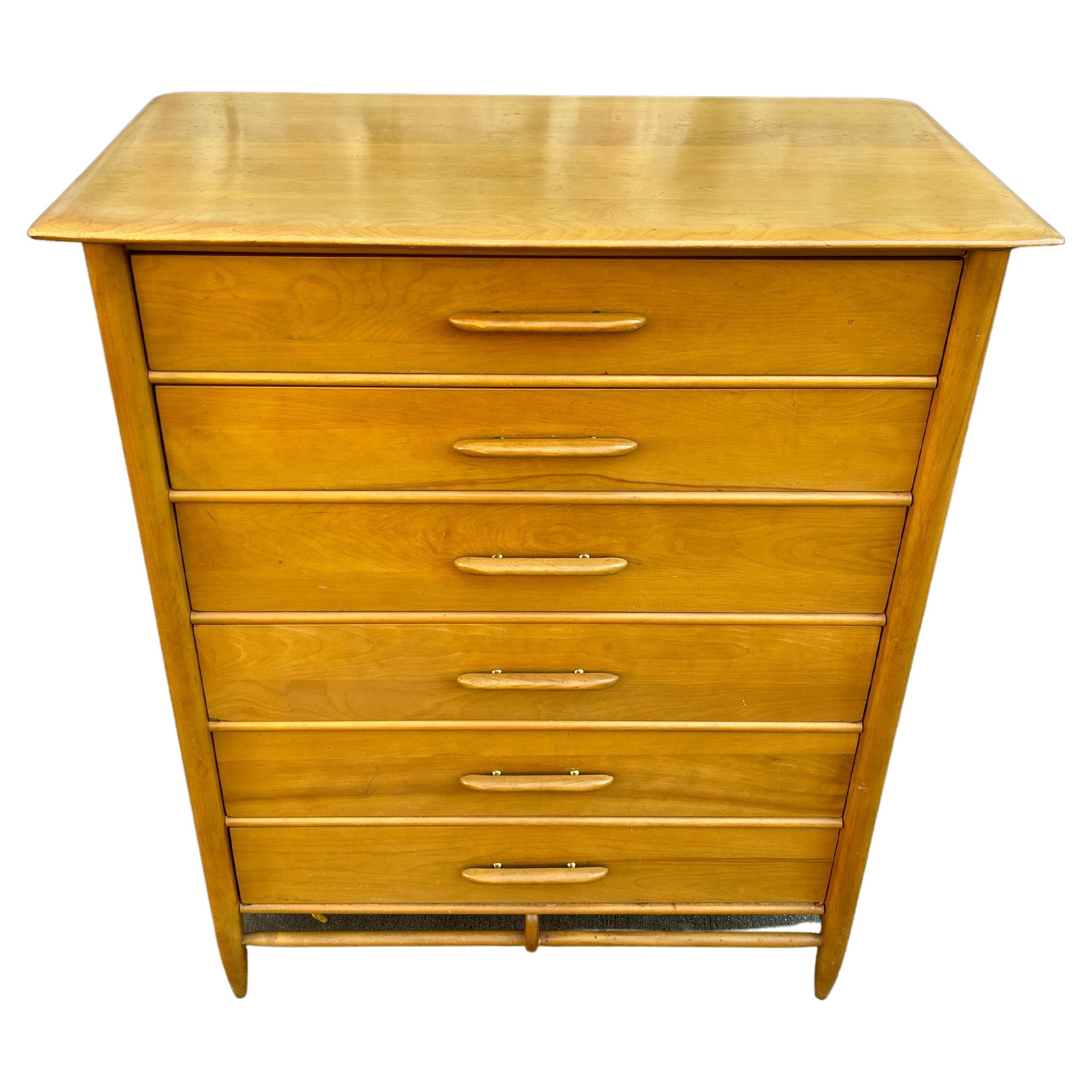 Comò alto a 6 cassetti in acero massiccio biondo, stile metà secolo moderno. Ha dettagli curvilinei con gambe a spina dorsale affusolate. Maniglie in acero intagliato con dettagli in ottone. Cassetti in acero massiccio con incastri a coda di