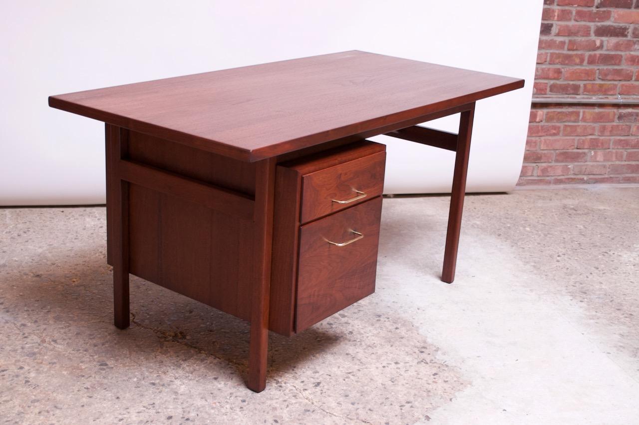 1950s American desk crafted in walnut with brass pulls. Features a two-drawer 'floating cabinet' which provides a shallow top drawer with removable divider and a second sizable lower drawer / filing cabinet with a sliding plastic divider.
Finished