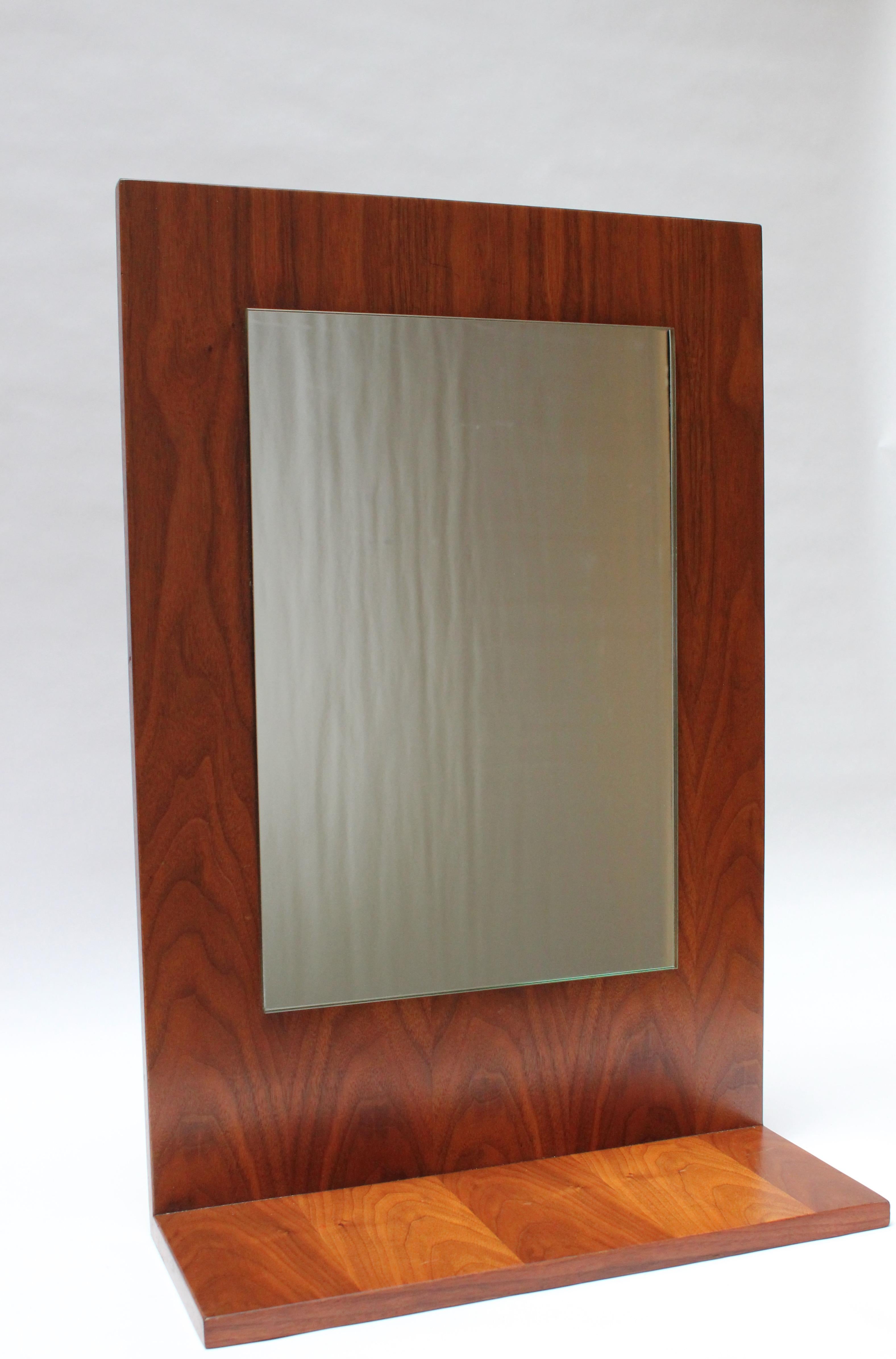 This American Modern walnut mirror can rest on a surface (supported by its shelf) or be mounted to a wall (the wire has been added, so the mirror is in ready to hang condition). The back is unfinished, and the piece is in good, vintage condition