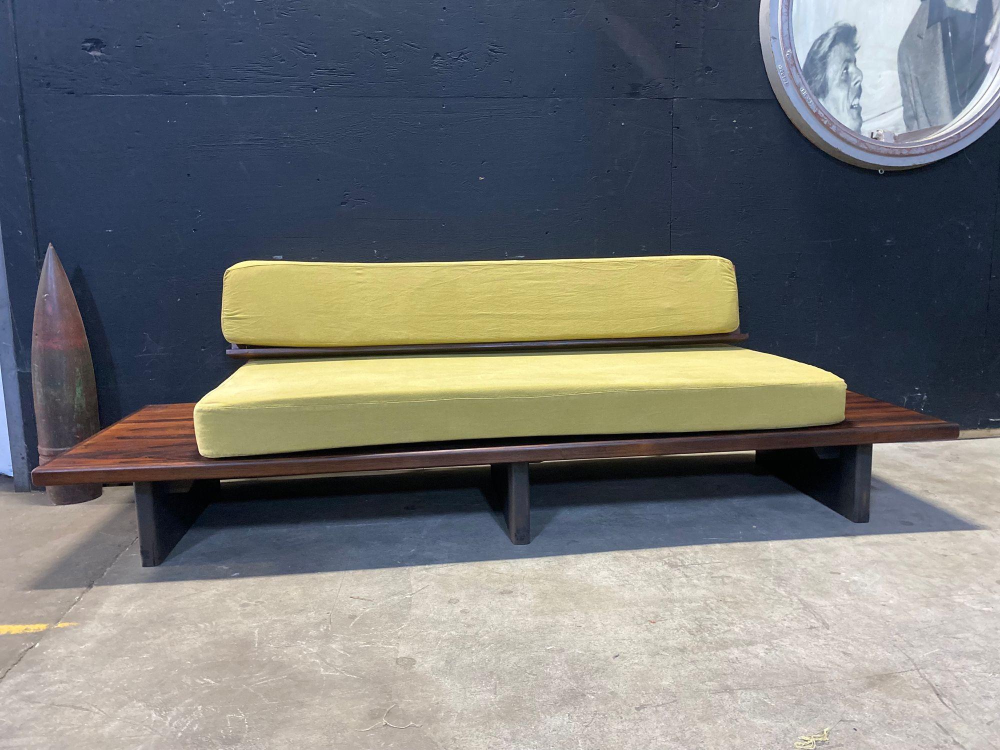 This is a beautifully made 1950's daybed in gorgeous rosewood with ochre linen upholstery. There is table space on either end for a lamp or a piece of art. the back is held up by beautiful curved polished steel. it sits on three black slab style