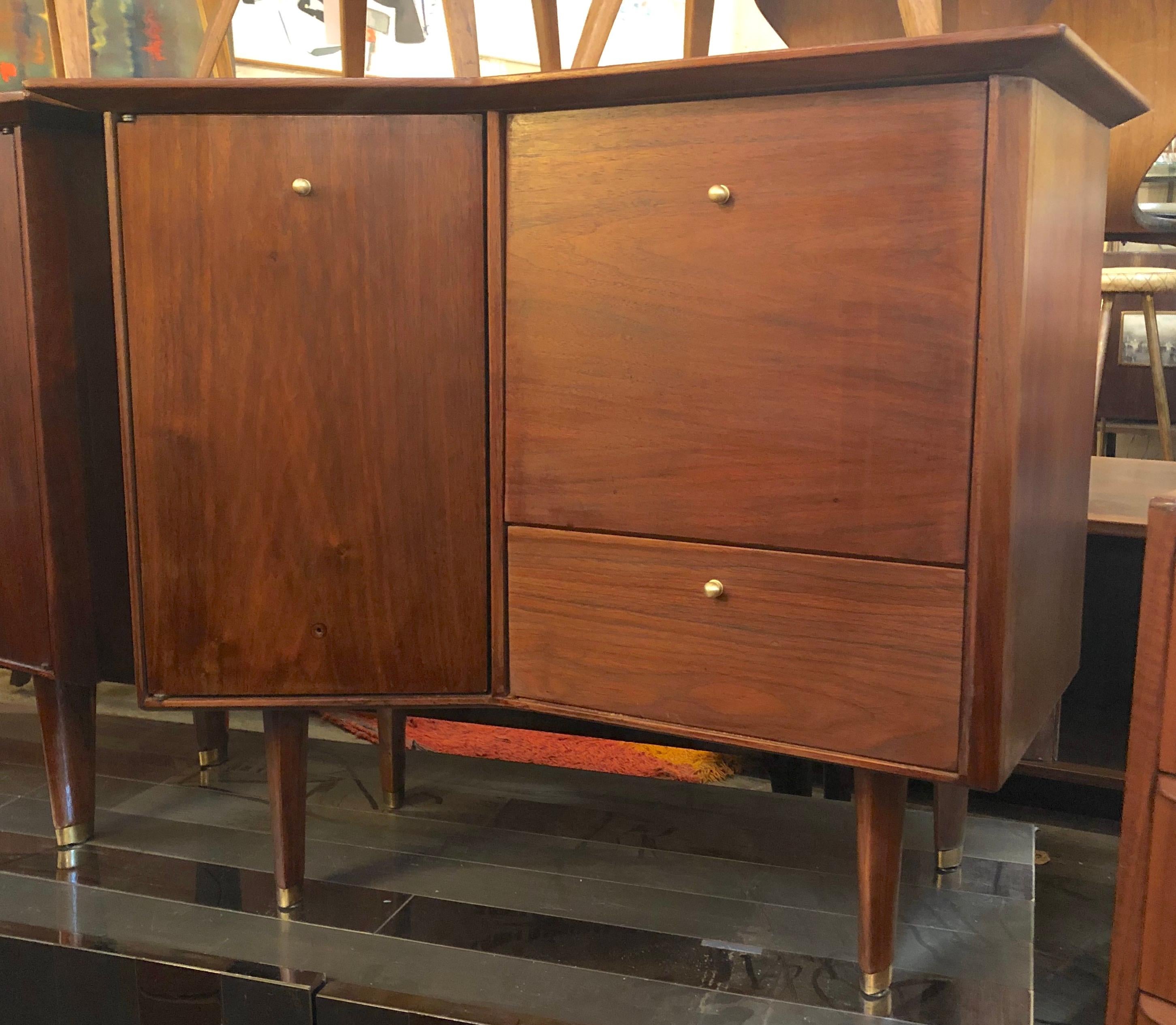 Stylish midcentury nightstands by Baker Furniture Co. Unusual design featuring angled tabletops, ample storage space, drop-down cabinets, brass accents on the feet and a sturdy walnut construction. 
Location: Brooklyn NY