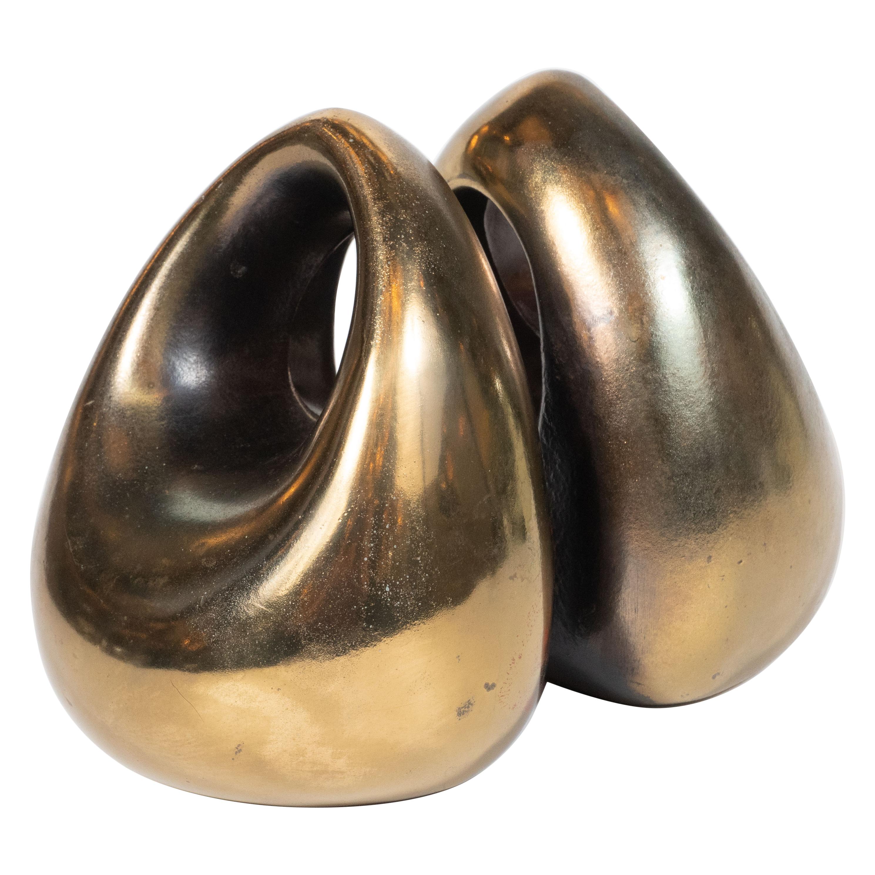 This elegant pair of book ends were realized by the esteemed Ben Seibel for Jenfred-Ware, circa 1950. They feature tear drop forms in glazed ceramic that come to an arched apex above a circular cut- all realized in a lustrous antiqued brass enamel