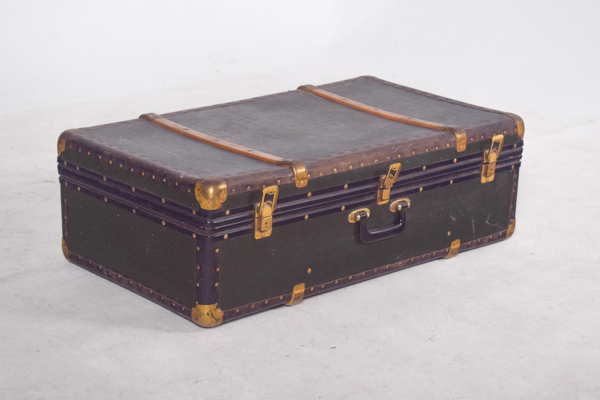Valigia antica rivestita in tessuto acrilico verde con finiture in ottone placcato oro su bordi, angoli e chiusure. La struttura è rinforzata con borchie su tutto il perimetro, che le conferiscono robustezza e carattere decorativo. Ha una maniglia