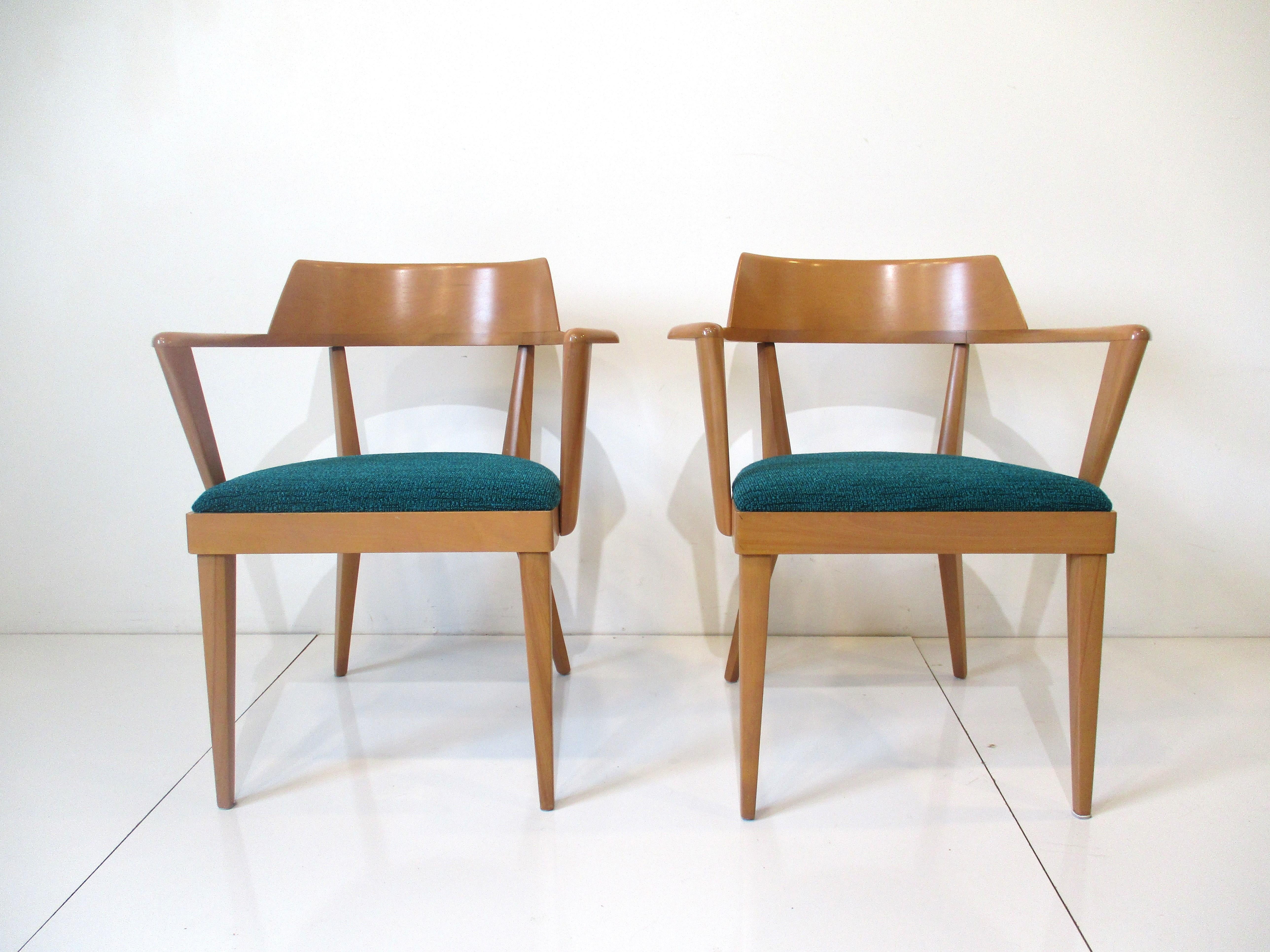 A pair of very well crafted solid maple wood arm chairs with great wood grain and in the original sea blue green fabric . Designed by Leo Jiranek and Ernest Herrmann having a curved backside and arms that are stylishly jetting outward  giving the