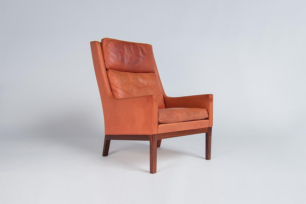 A beautiful high back armchair in leather and rosewood designed by Kai Lyngfeldt Larsen for Soren Willadsens in Denmark 1950’s. Beautiful lovely rich amber tones to the original patinated leather upholstery complemented nicely by the rosewood base.