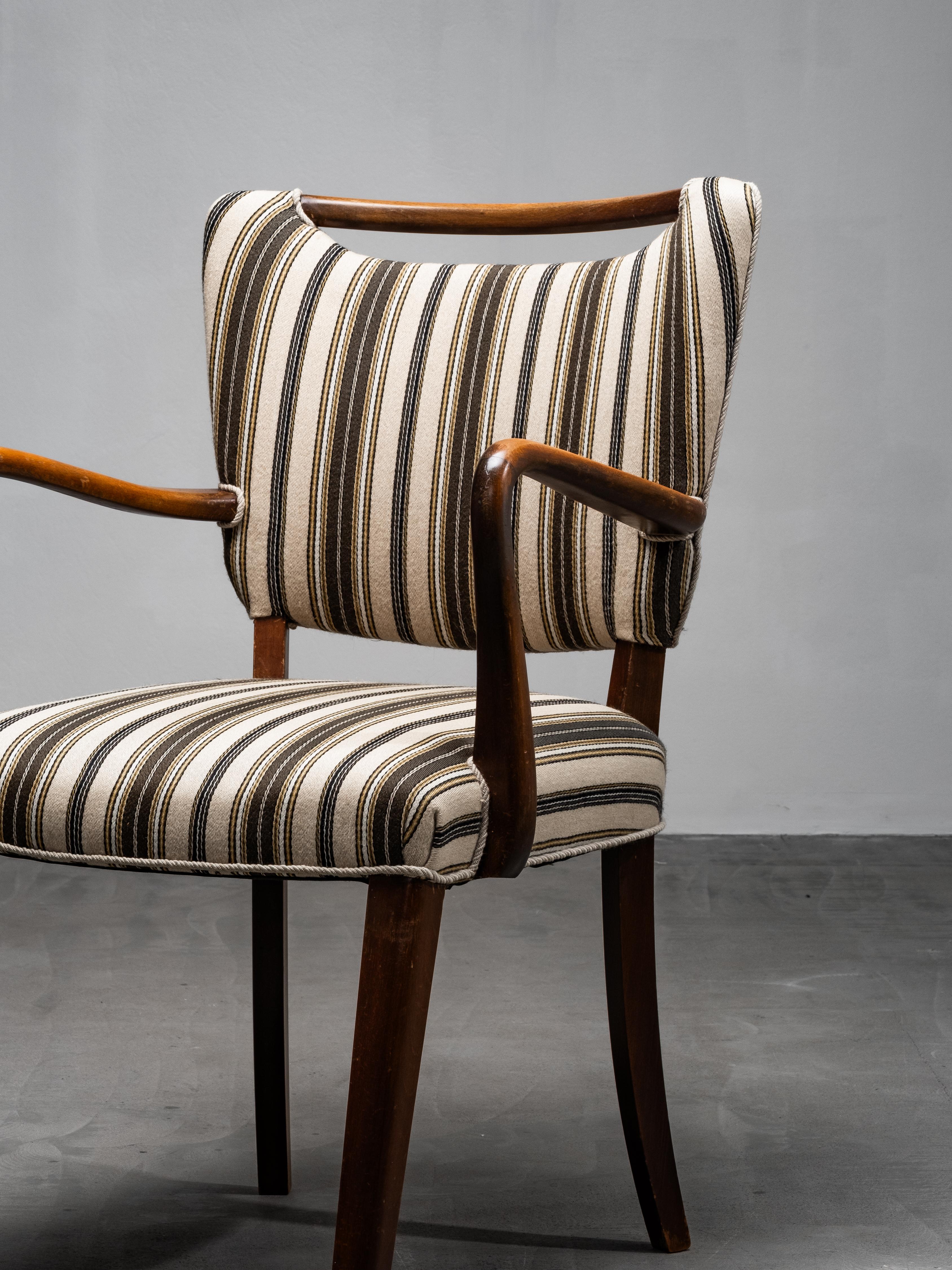 An elegant mid-century armchair in stained beech, retaining its original striped wool upholstery in warm tones of brown, black, and cream. The gently curved arms, sculpted backrest and tapered legs express a soft, organic modernism typical of