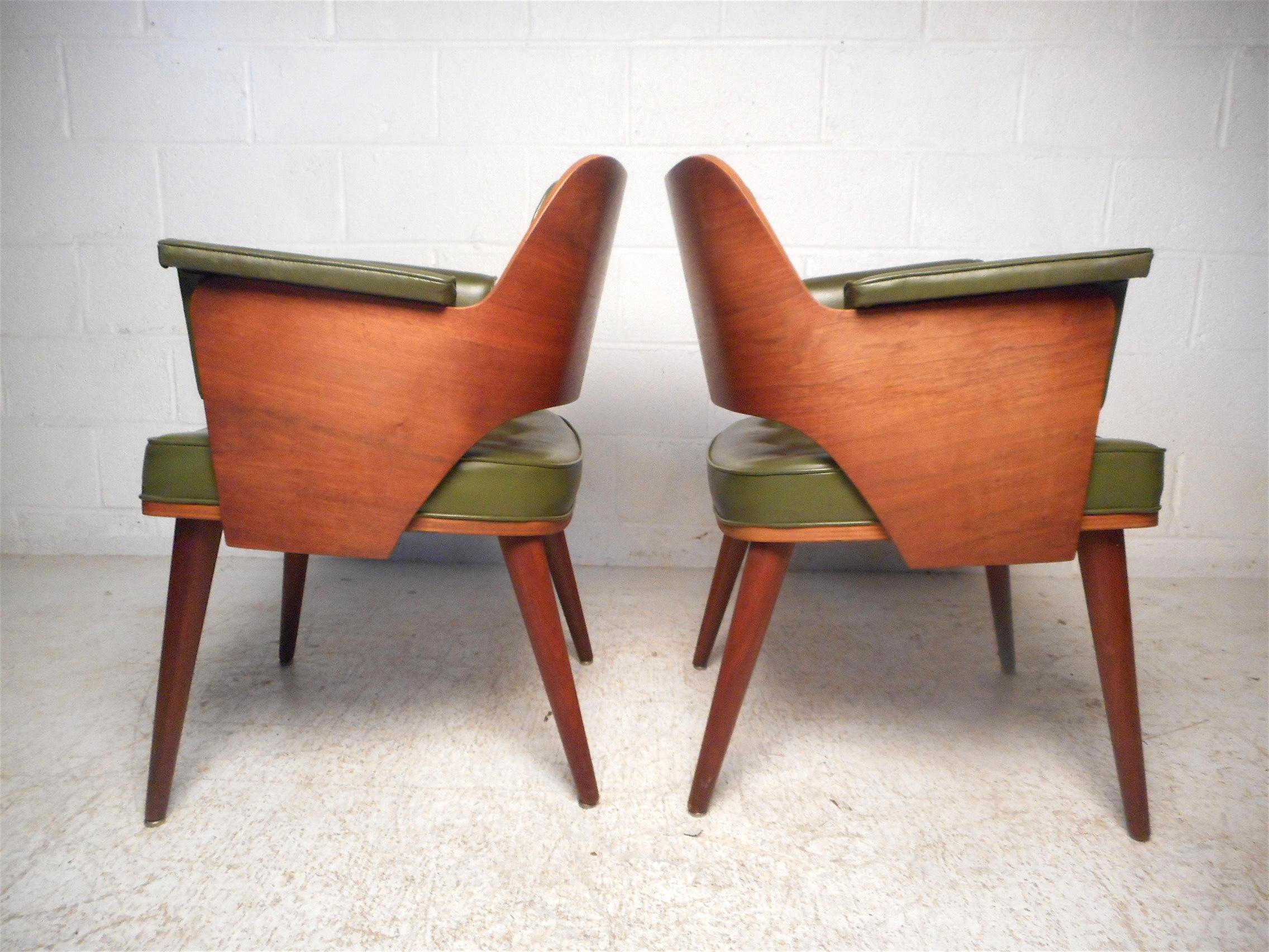 Stylish and unusual pair of midcentury chairs by Taylor Chair Co. Sculpted wooden backrests along with splayed and tapered legs give these chairs a striking visual profile. Covered in a vintage green tufted faux-leather upholstery. Great pair of