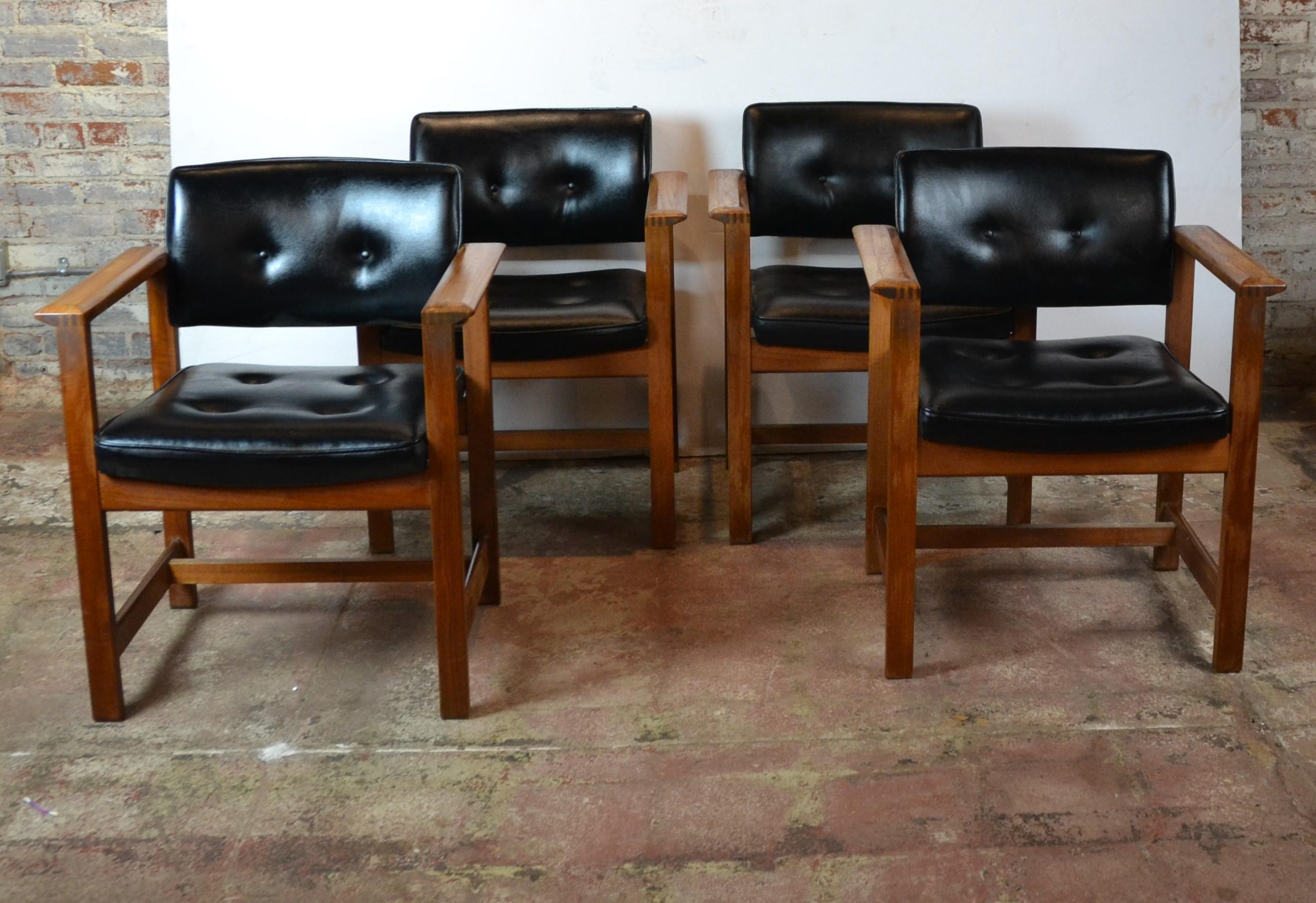 Set of four midcentury armchairs. The arms have detail workmanship with teak wood. The chairs are covered in black faux-leather.