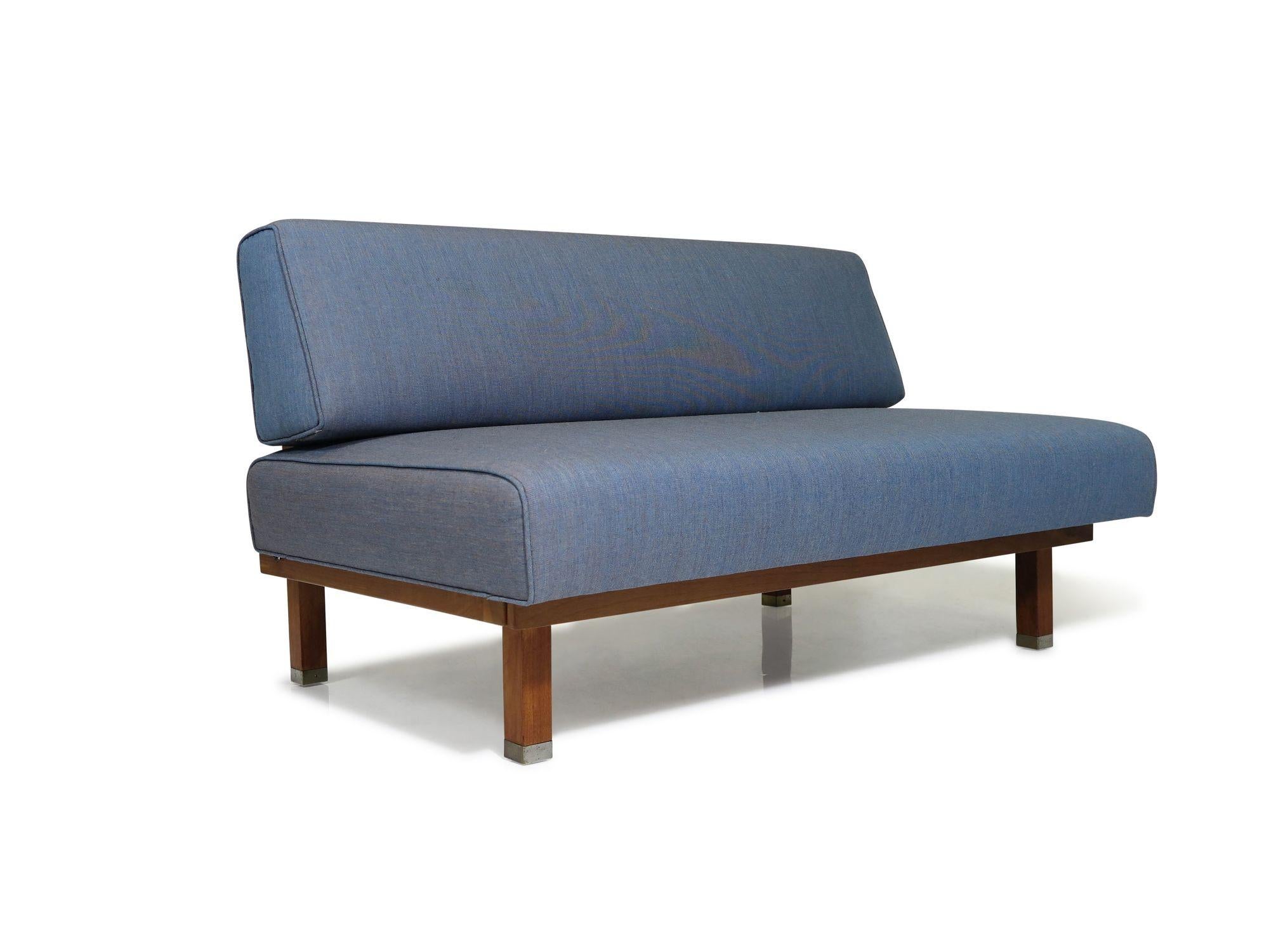 Mid-Century armless settee crafted with a solid walnut frame, newly upholstered in a classic blue textile, raised on squared legs with brass caps. The loveseat is in excellent condition, displaying only minor signs of age and use.

Measurements
W