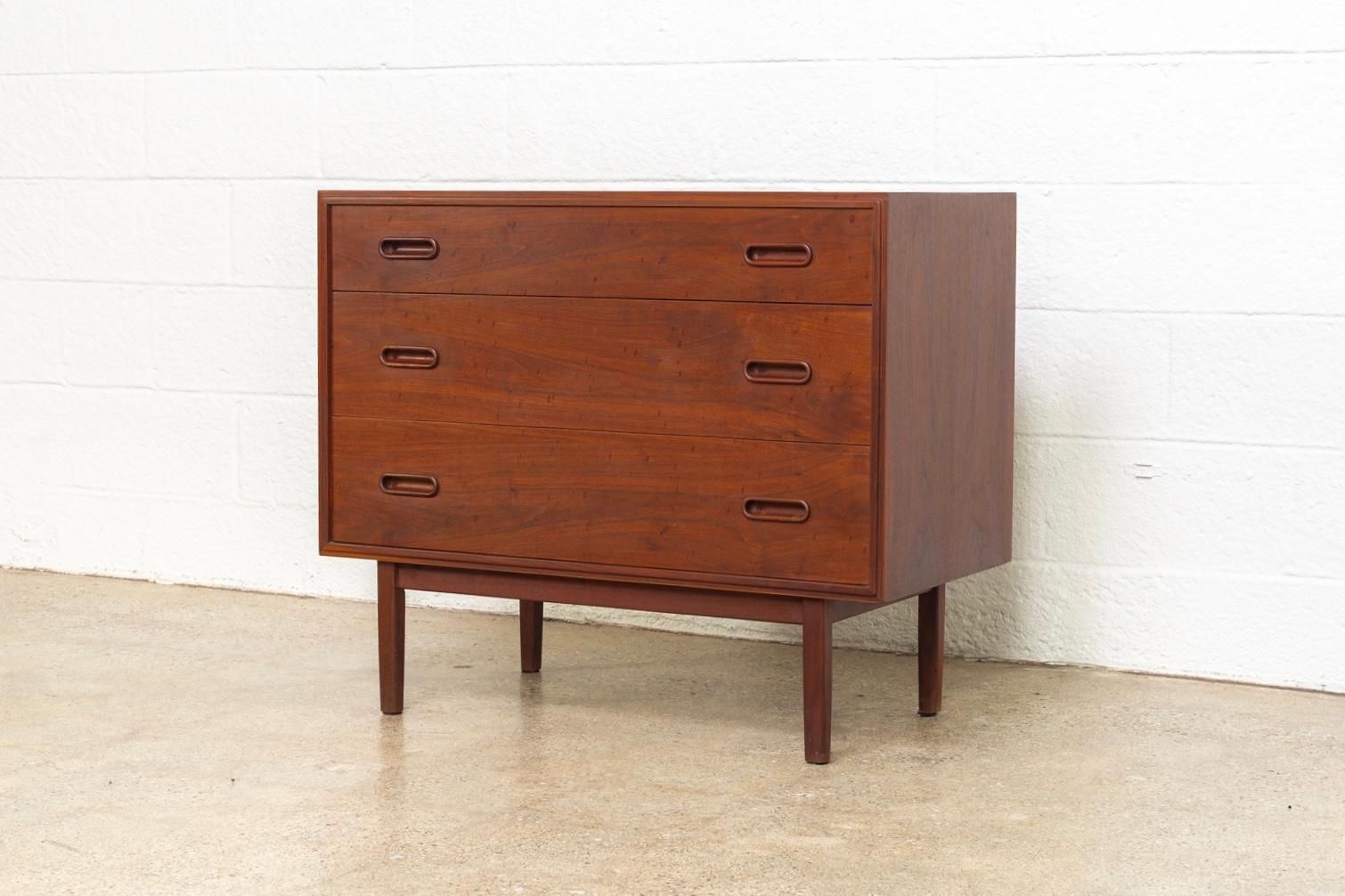 This vintage midcentury Danish modern three-drawer dresser in the manner of Arne Vodder is circa 1960. The Classic Danish modern design has elegant, Minimalist styling featuring distinctive sculptural drawer pulls and squared-off legs. It is