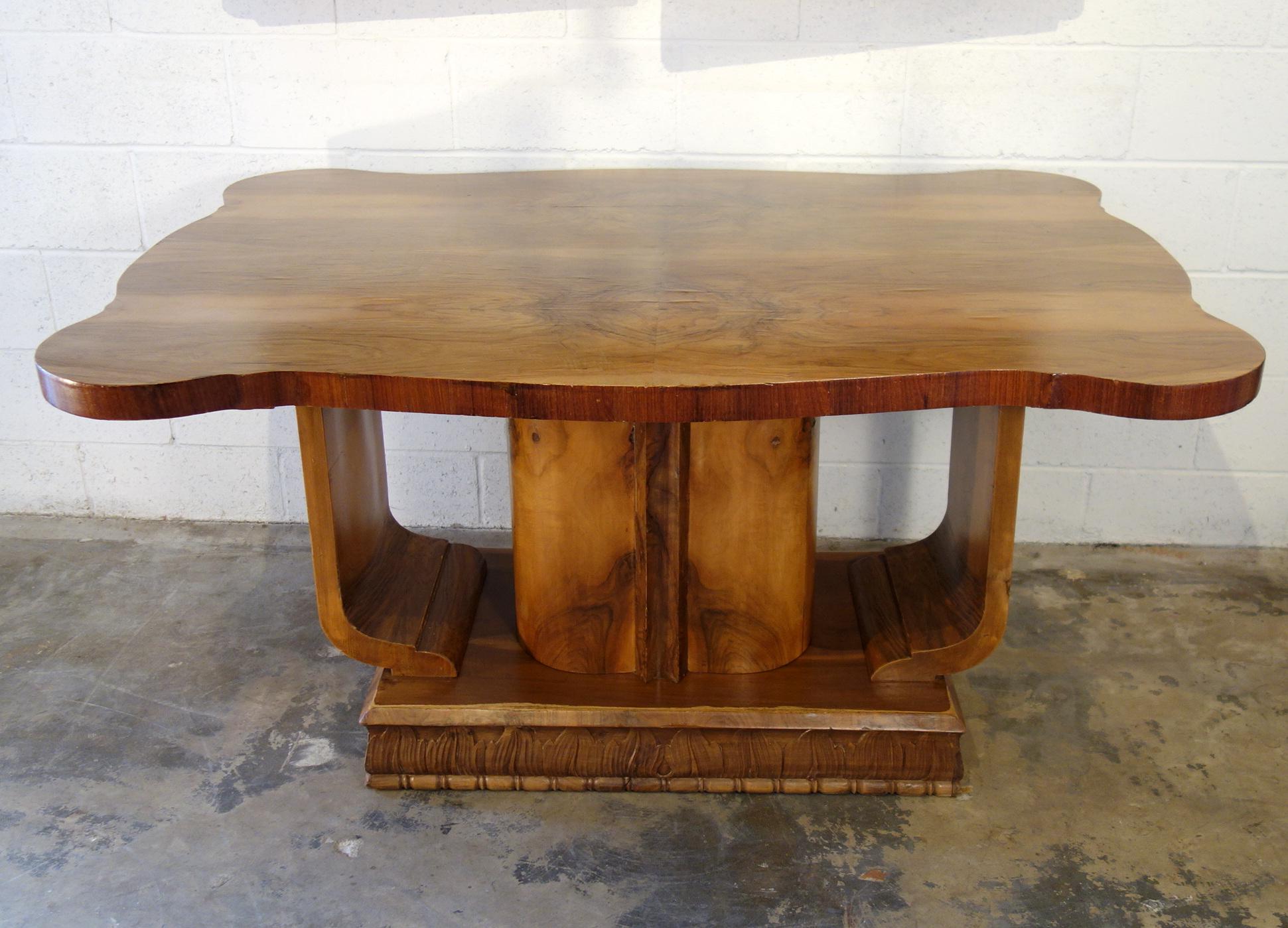 A playful, decorative Art Deco entrance table features a symphony of book match and butterfly patterns composed of walnut burl veneers. The structural orchestration involves an oval central column within arched side pedestal supports, all rising