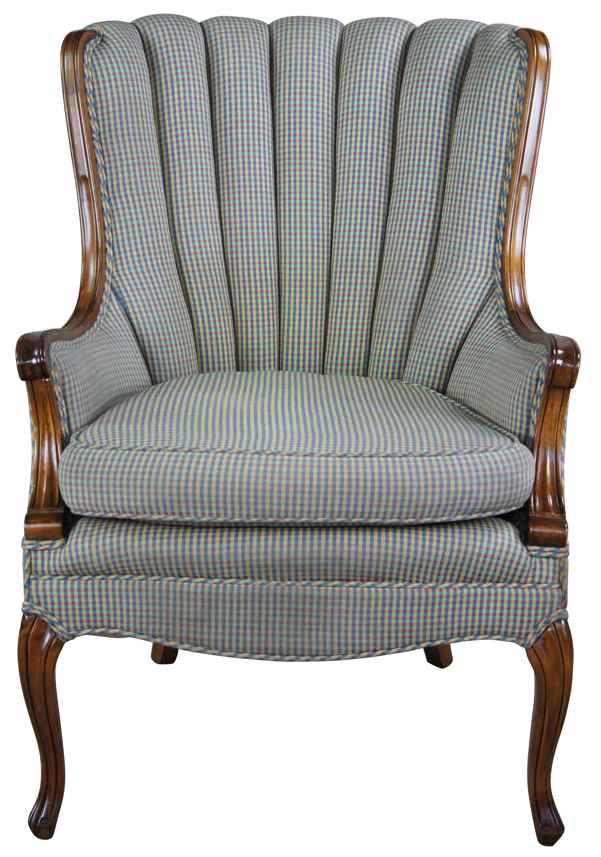 Mid century upholstered walnut armchair featuring serpentine form with flared wingback and channel back design, plaid upholstery and fluted accents. Measures: 38