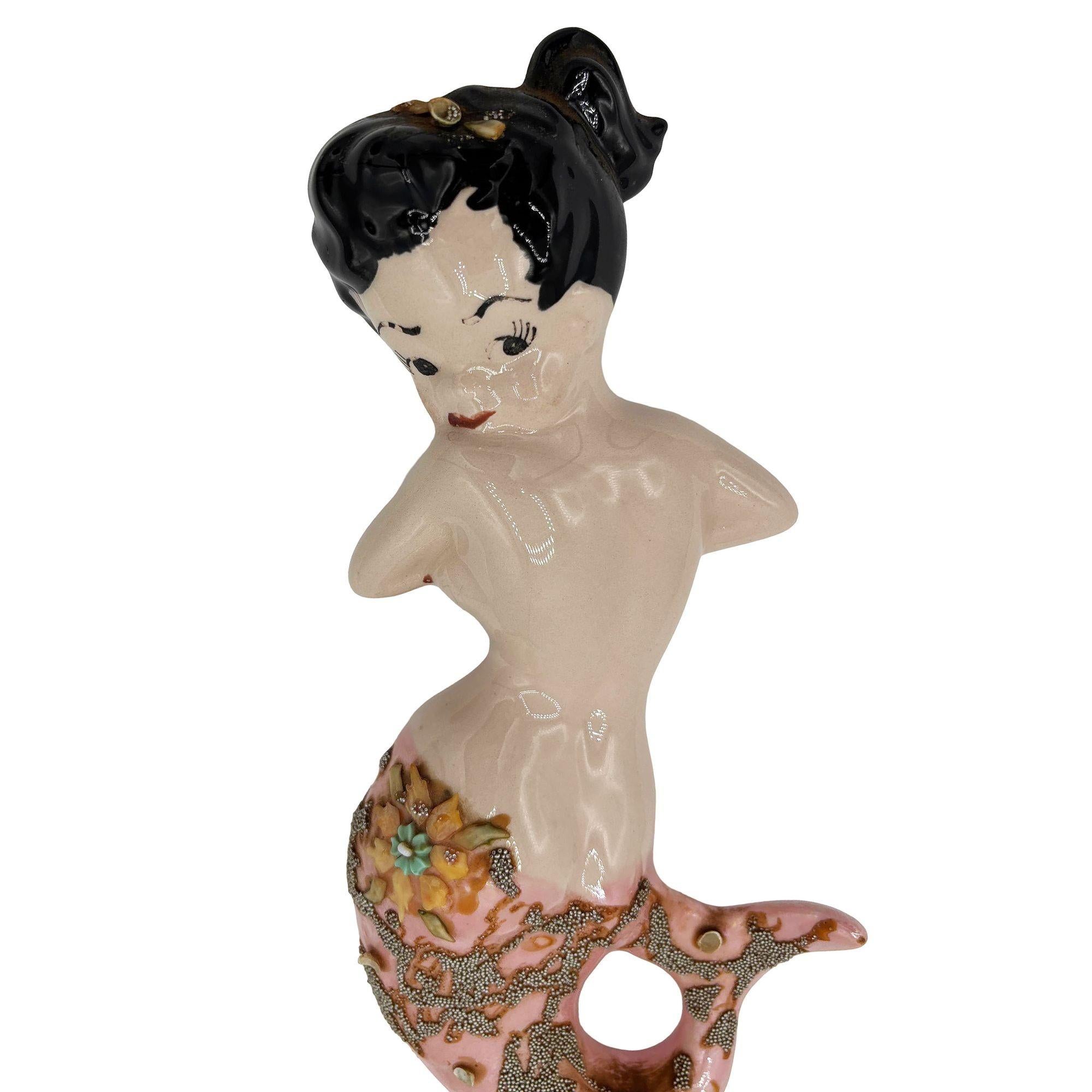 Sculpture murale originale en céramique du milieu du siècle, avec un design classique inspiré des pin-up, une brune aux cheveux attachés en queue de cheval, une pose effrontée au-dessus de l'épaule et une queue rose scintillante avec des détails