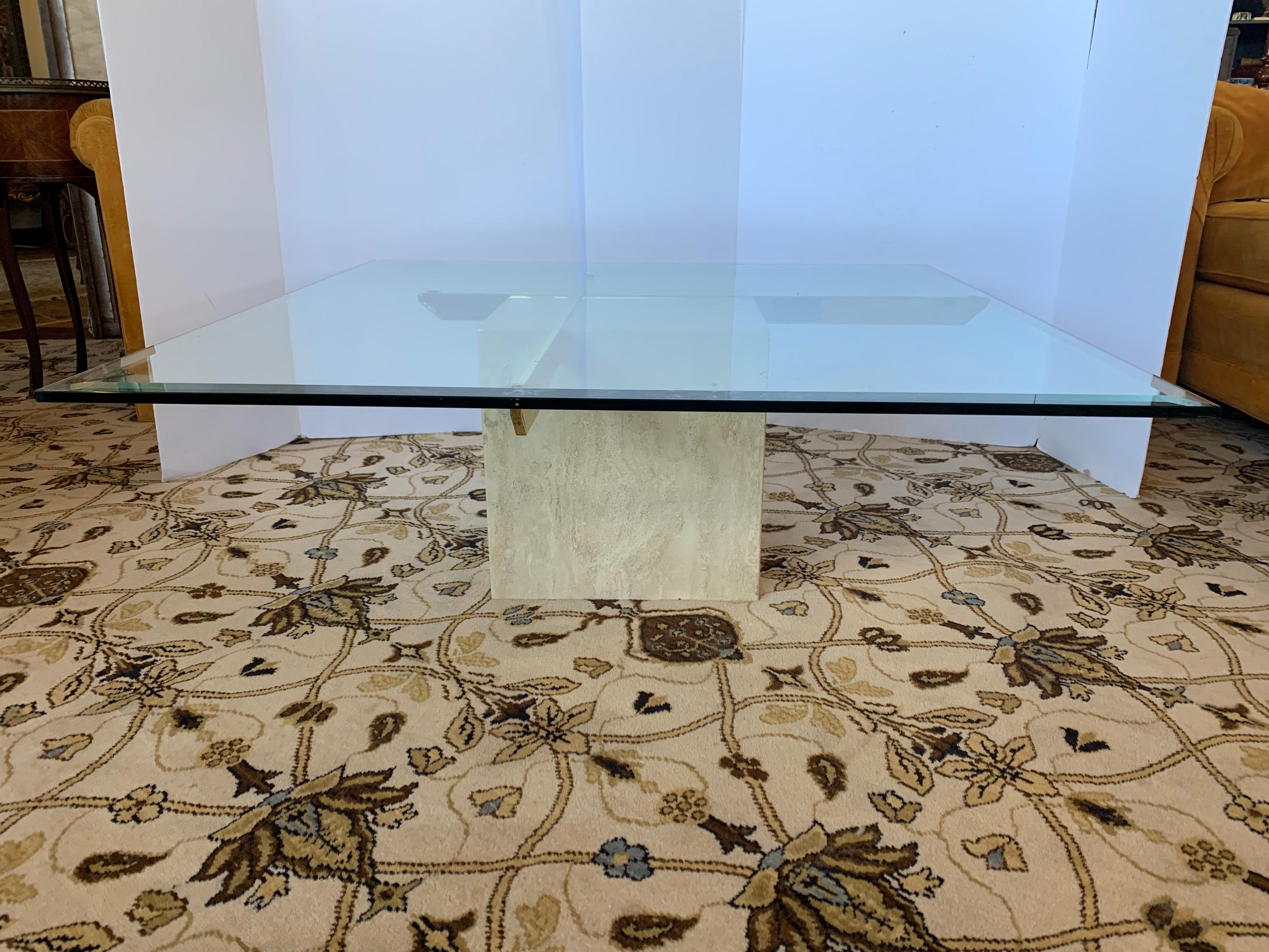 Magnificent Mid-Century Modern Artedi coffee table features a thick square glass top with a travertine base. Sleek design with two brass supports fitted inside the travertine marble base holds the large glass tabletop. This elegant piece makes the