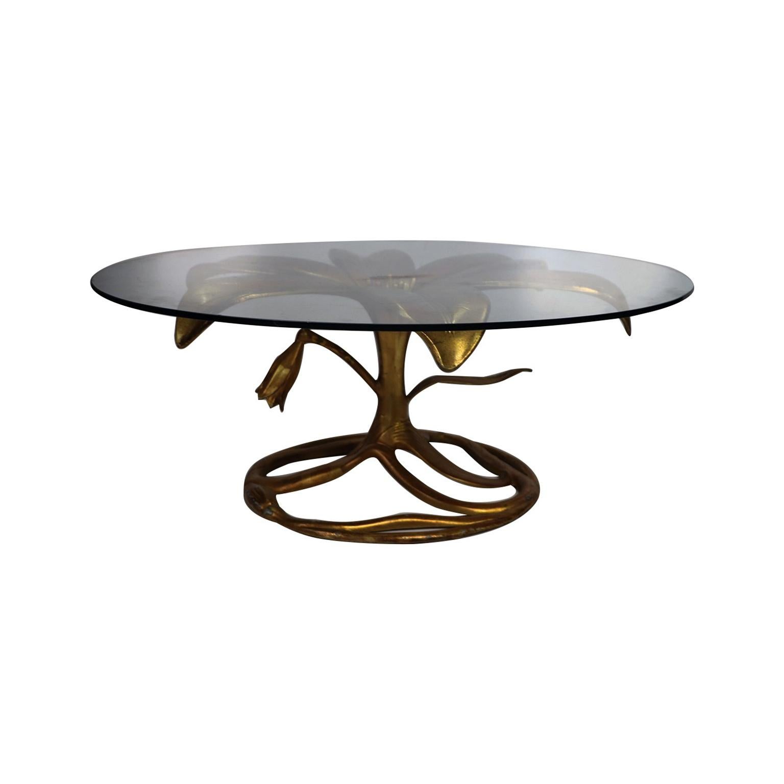 Stunning gilded lily cocktail table with circular glass top by Arthur Court, circa 1970s. This eye-catching conversation piece features a gold cast aluminum base with an open lily bloom supporting a thick glass top above a closed bloom and leaf