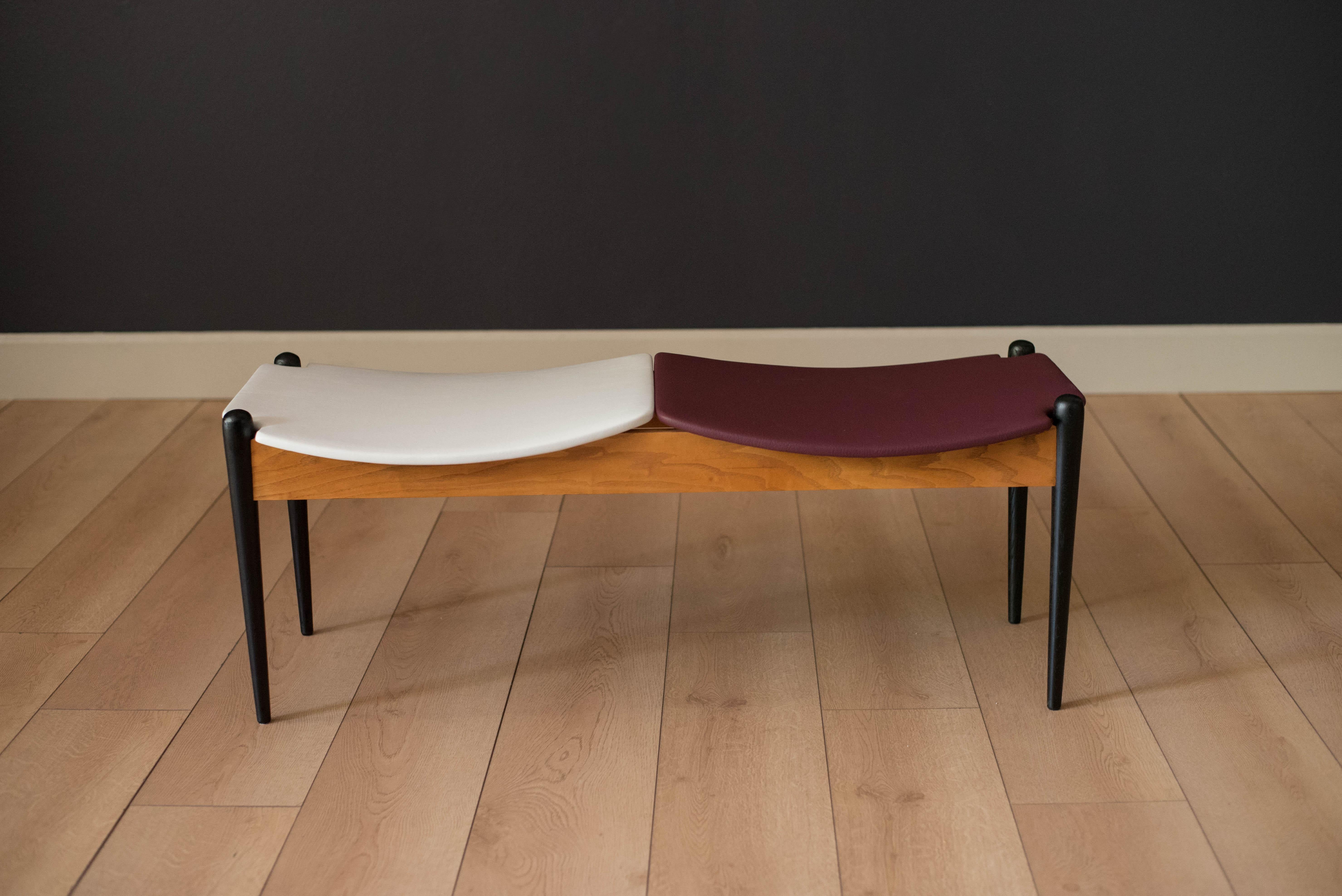 Classic Mid-Century Modern designed bench by Arthur Umanoff for Washington Wood Prod. Inc. This versatile piece features two-tone double seating reupholstered in white and maroon vinyl. Perfect to use as an entryway or bedside bench.
 
