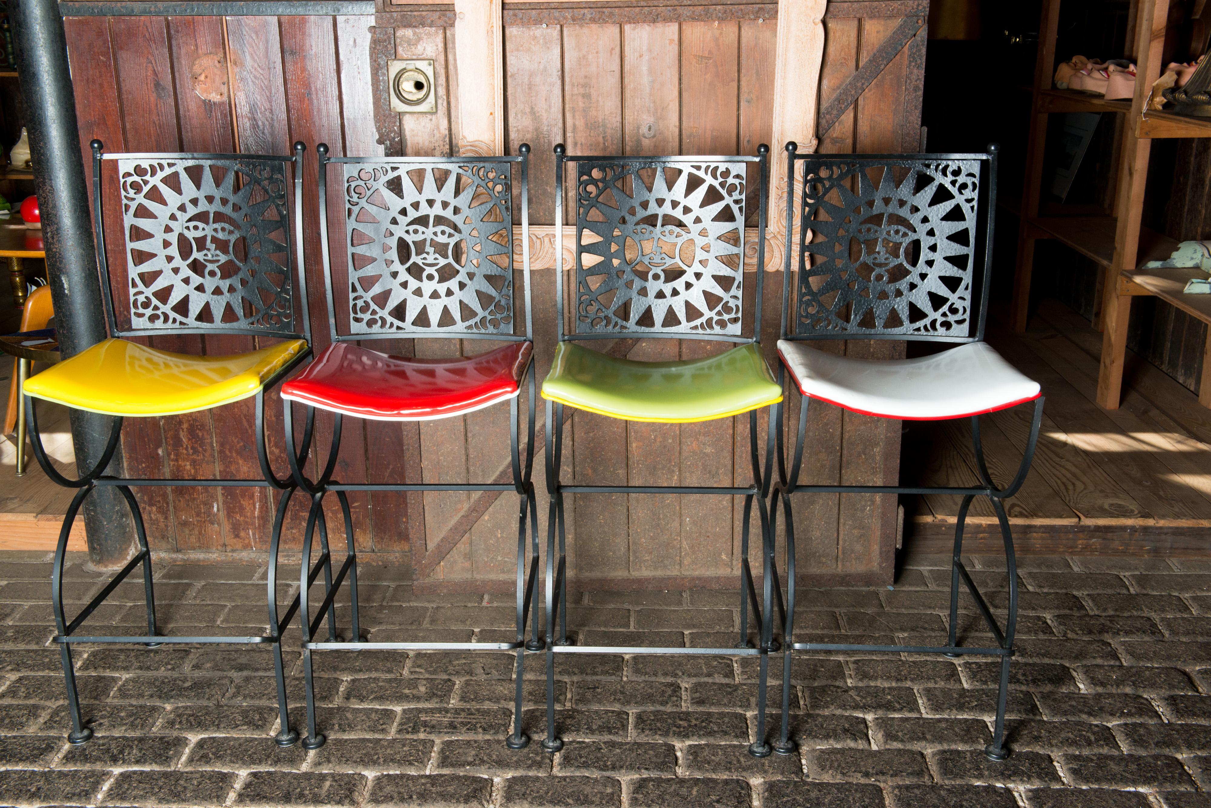 A set of four mid-century Mayan sun face back iron bar stools by Arthur Umanoff for Shaver Howard. Two seats are red and white vinyl. Two seats are yellow and lime green. All are in very nice condition.